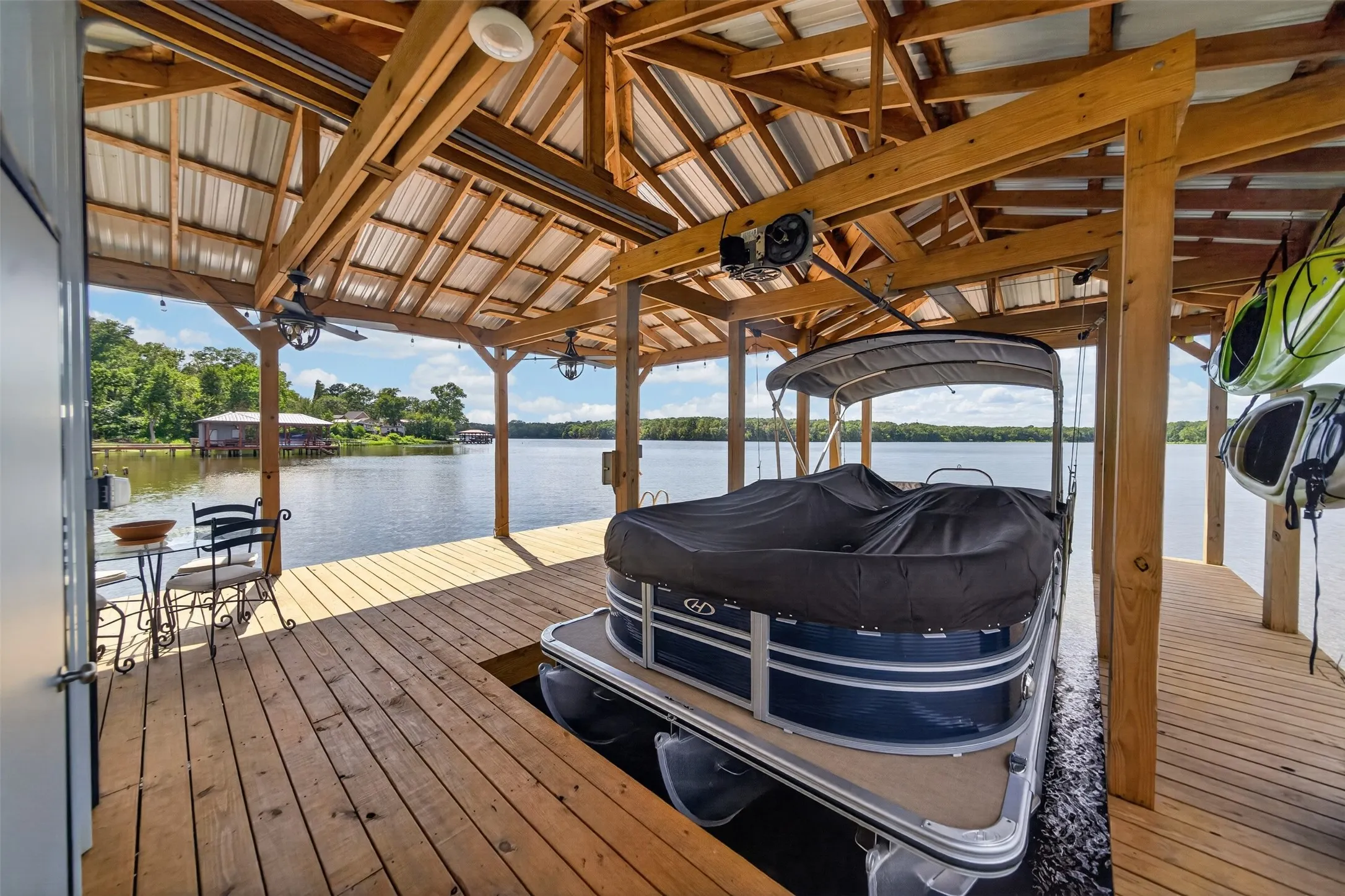 Waterfront boathouse with expansive covered dock featuring wood-finish decking, exposed beam ceiling with clerestory windows, and direct water access