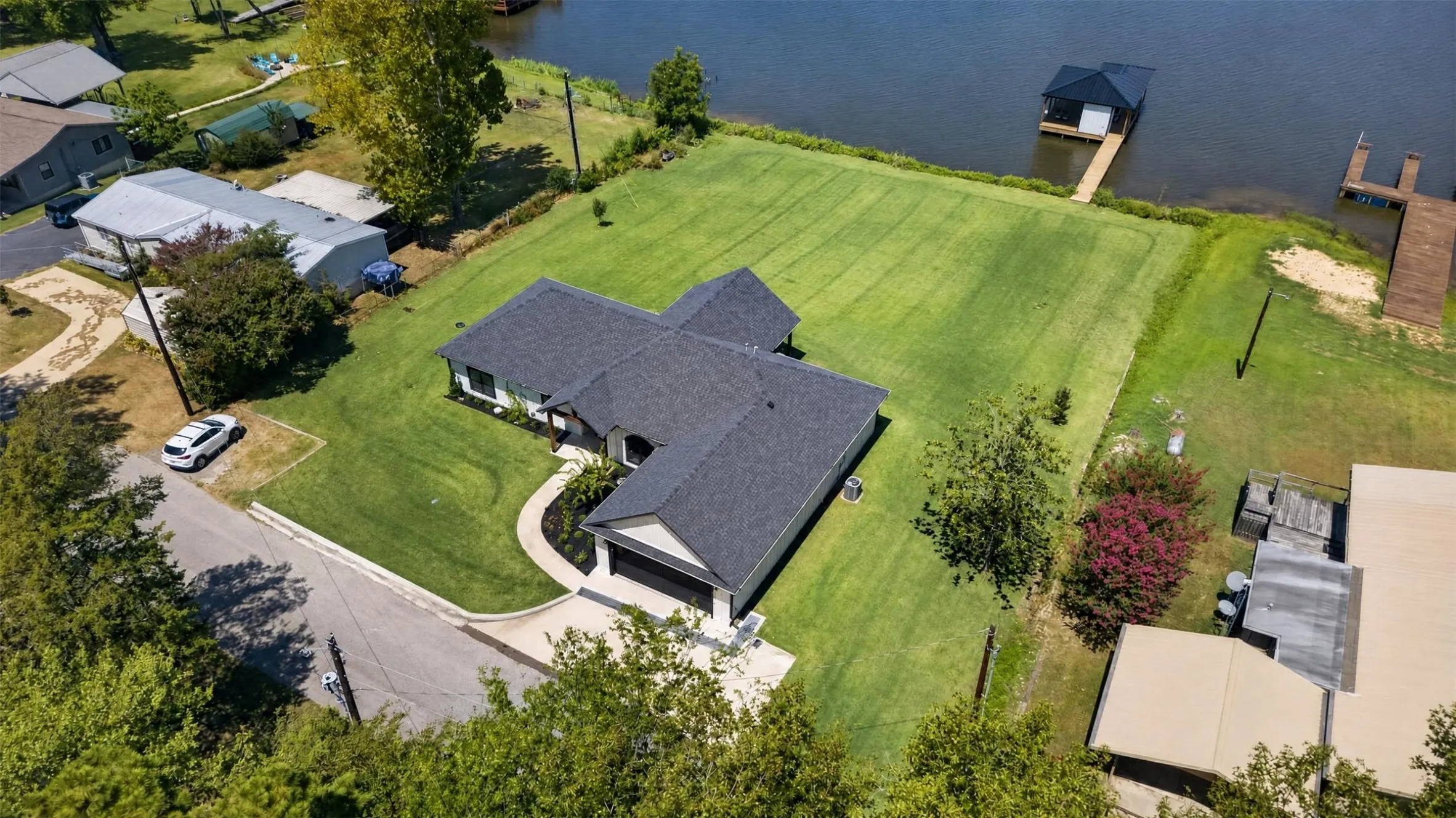 Waterfront property featuring a boat dock, boat house, expansive lawn, and mature landscaping