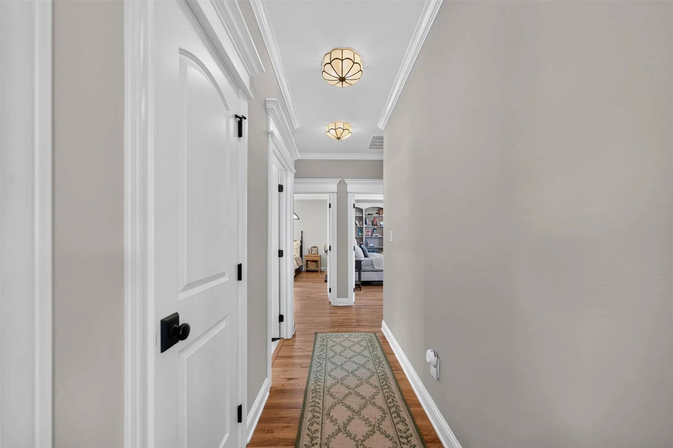 Hallway with hardwood flooring, crown molding, arched doorways, and two ceiling-mounted light fixtures