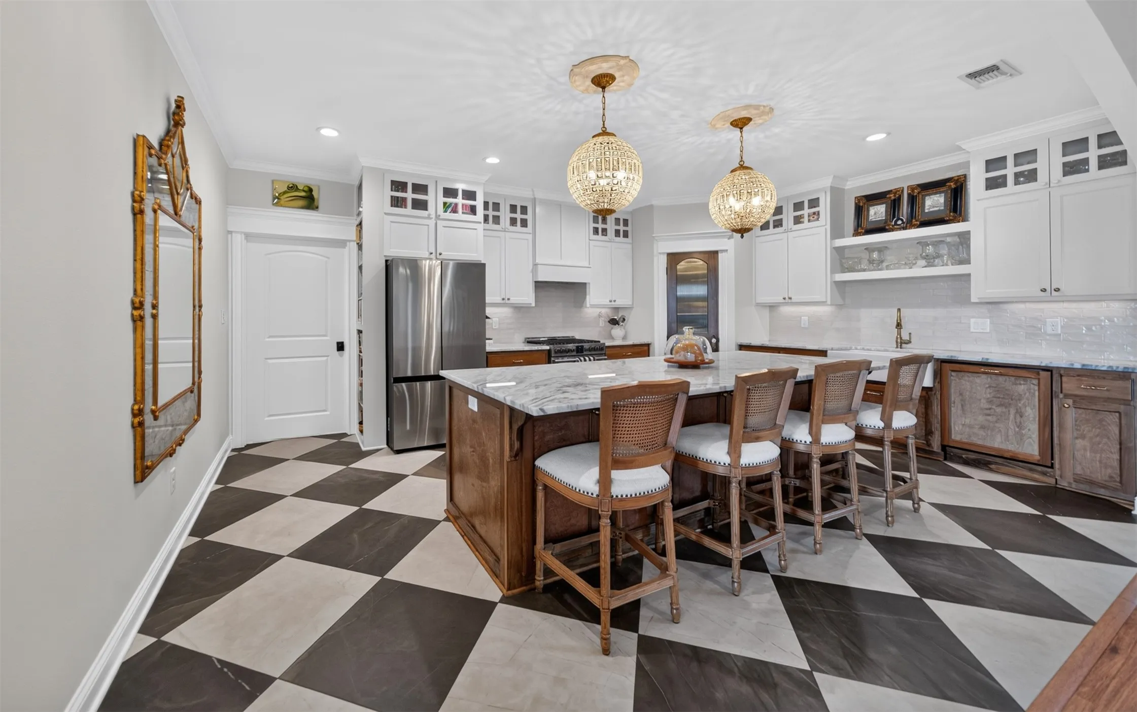 Spacious kitchen featuring checkerboard flooring, a large island with stone countertop, white upper cabinetry, stainless steel appliances, and decorative pendant lighting
