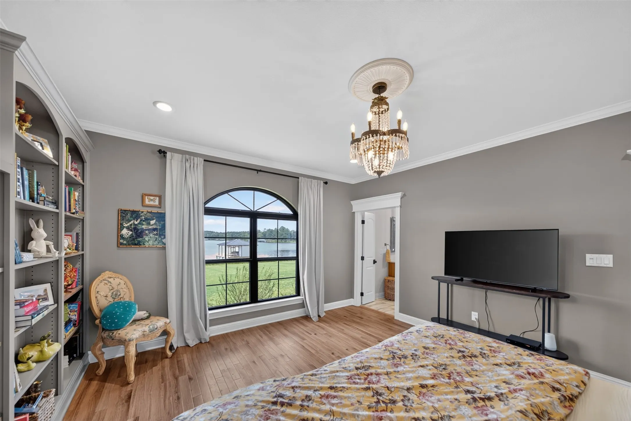 Spacious primary bedroom showcasing hardwood flooring, gray walls, and abundant natural light from an arched transom window