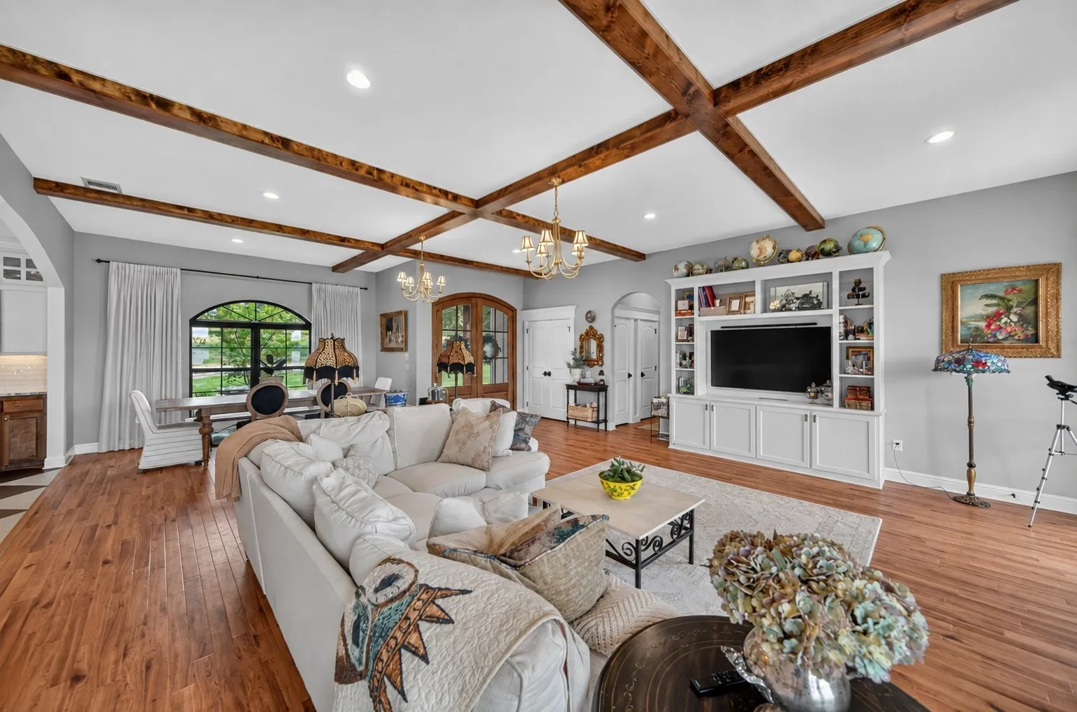 Wood-finish flooring, exposed ceiling beams, recessed lighting, built-in entertainment cabinetry, and an arched window