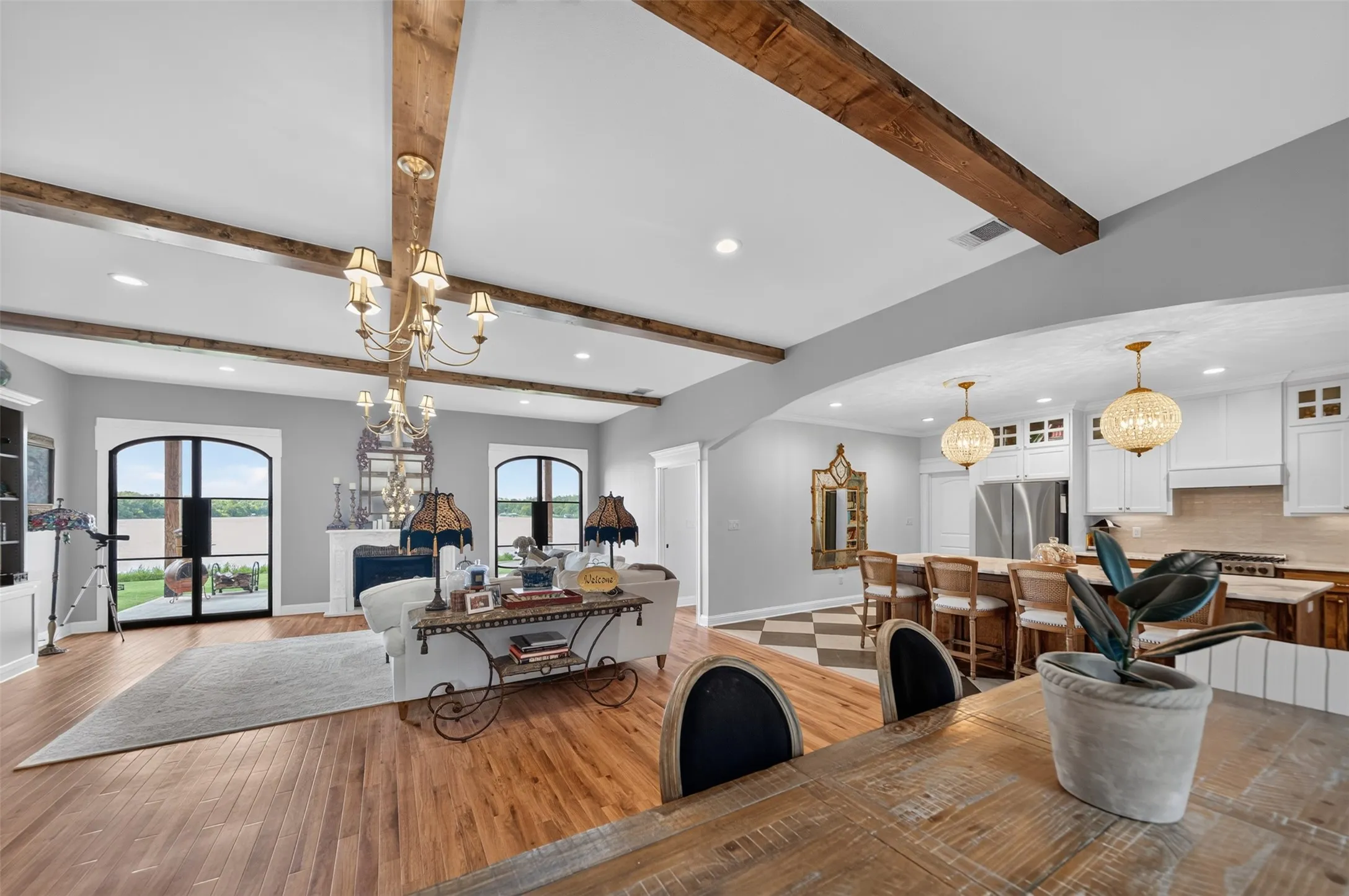 Hardwood flooring throughout, exposed wood beams, arched doorways, white cabinetry, and stainless steel appliances