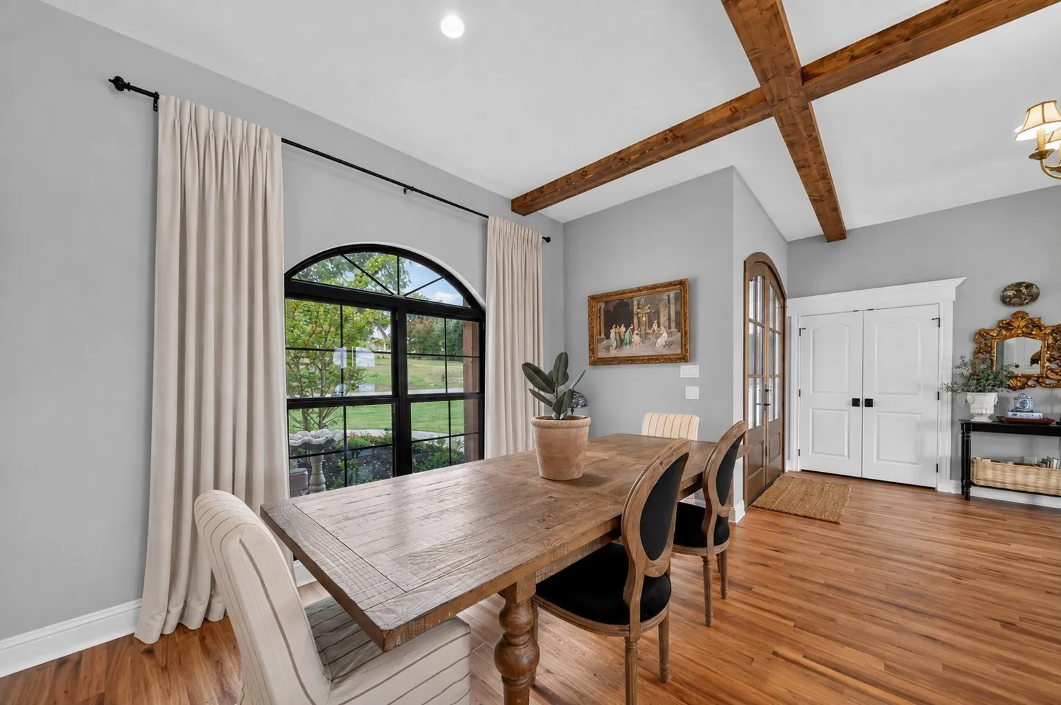 Arched window with black grid detailing, wood-finish flooring, exposed ceiling beams, and paneled double doors