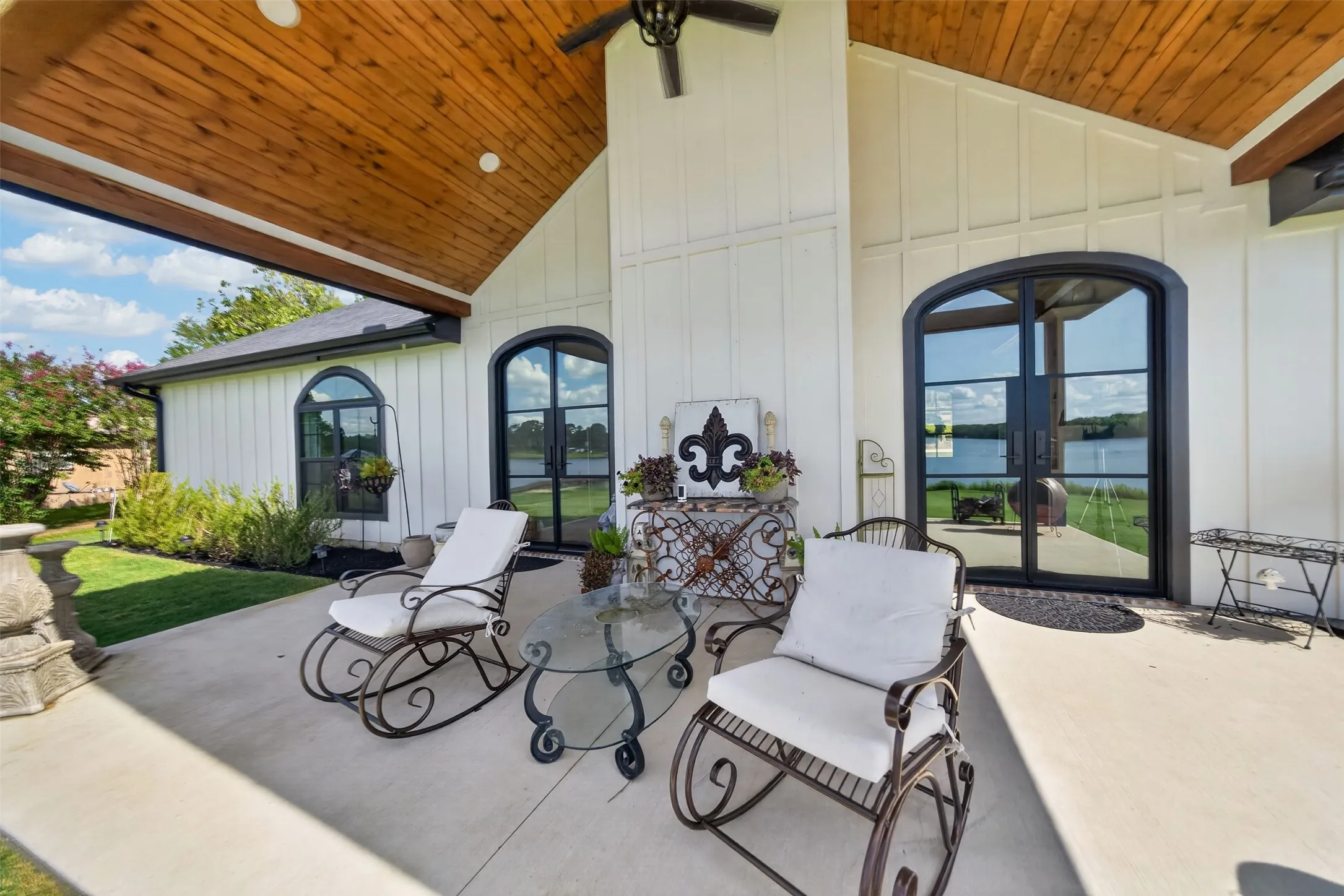 Covered patio with a wood-finish ceiling, board and batten siding, arched glass-panel doors, and arched windows