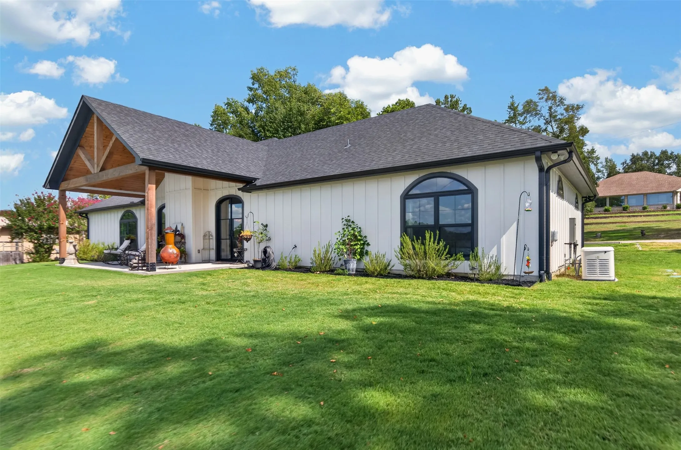 Expansive green lawn surrounds the home, featuring a covered patio with exposed wood beams and columns