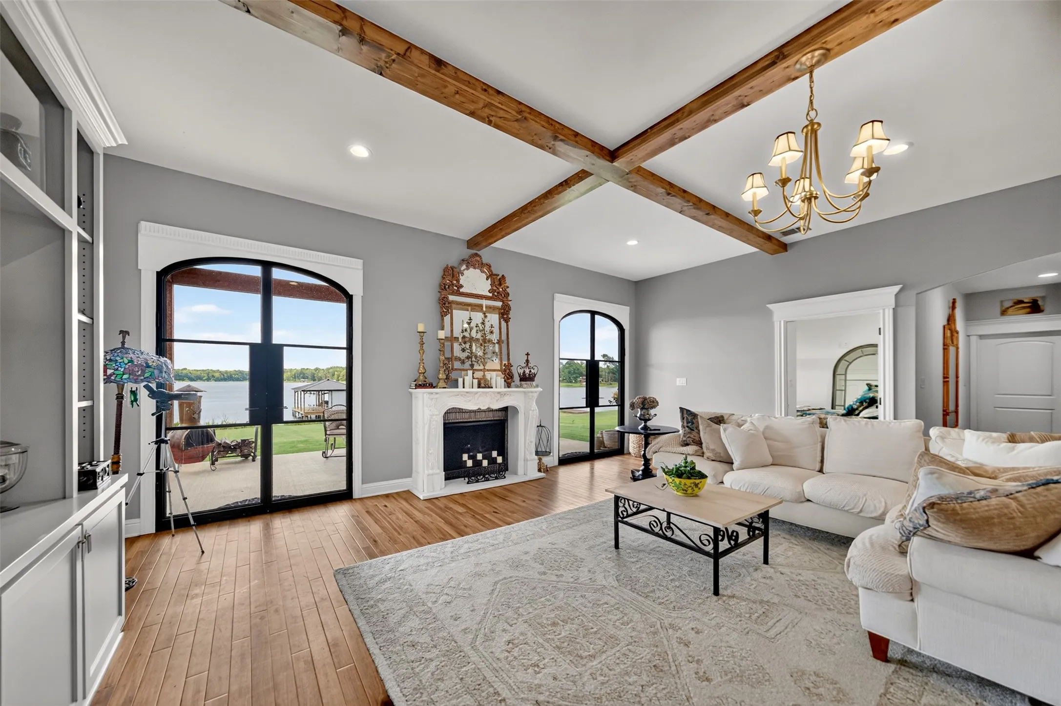 Spacious open-concept living room featuring exposed wooden ceiling beams, gray walls, and wood-finish flooring throughout
