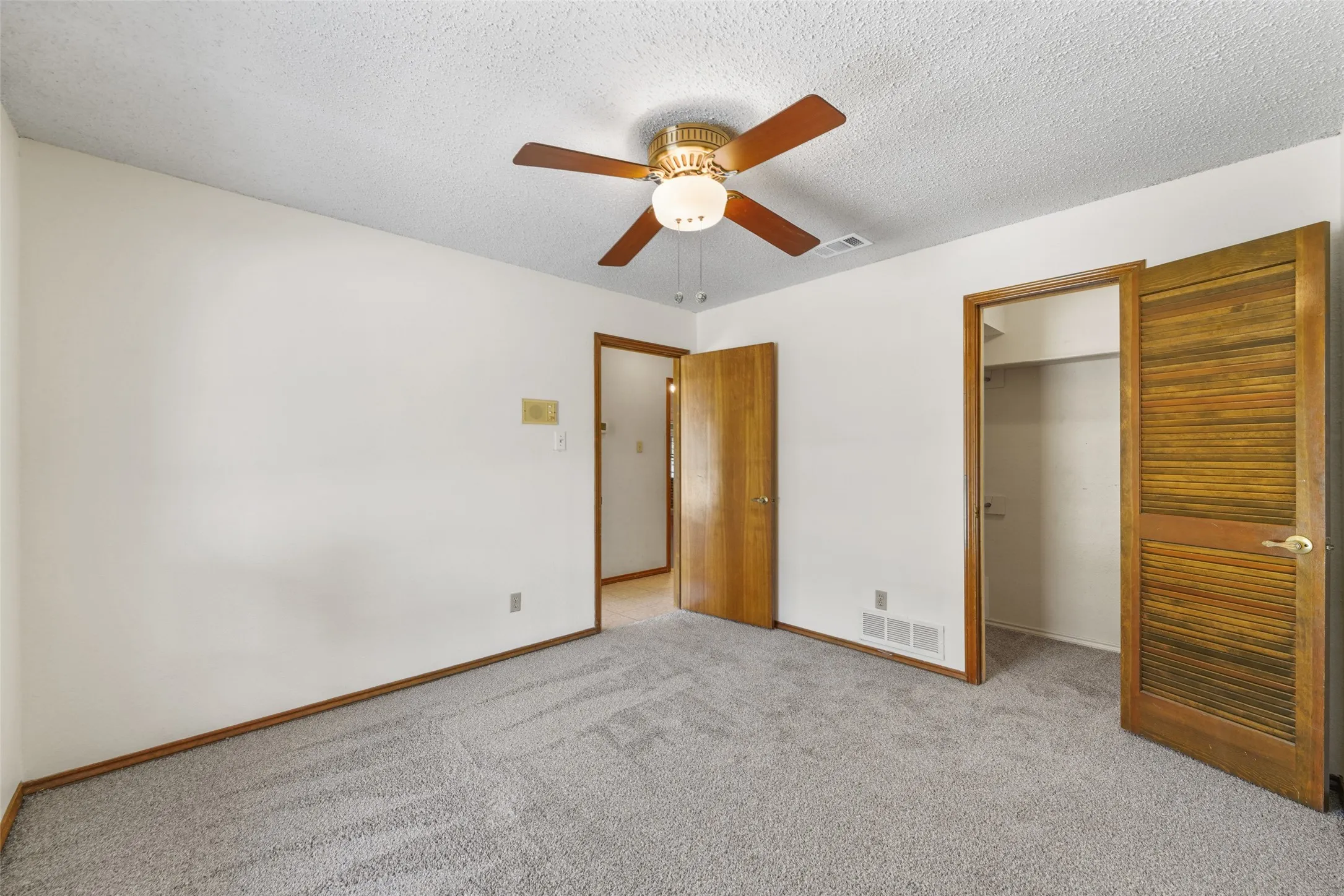 Ceiling fan with integrated lighting, textured ceiling, light gray carpet, wood-finish interior doors, and wood-finish trim