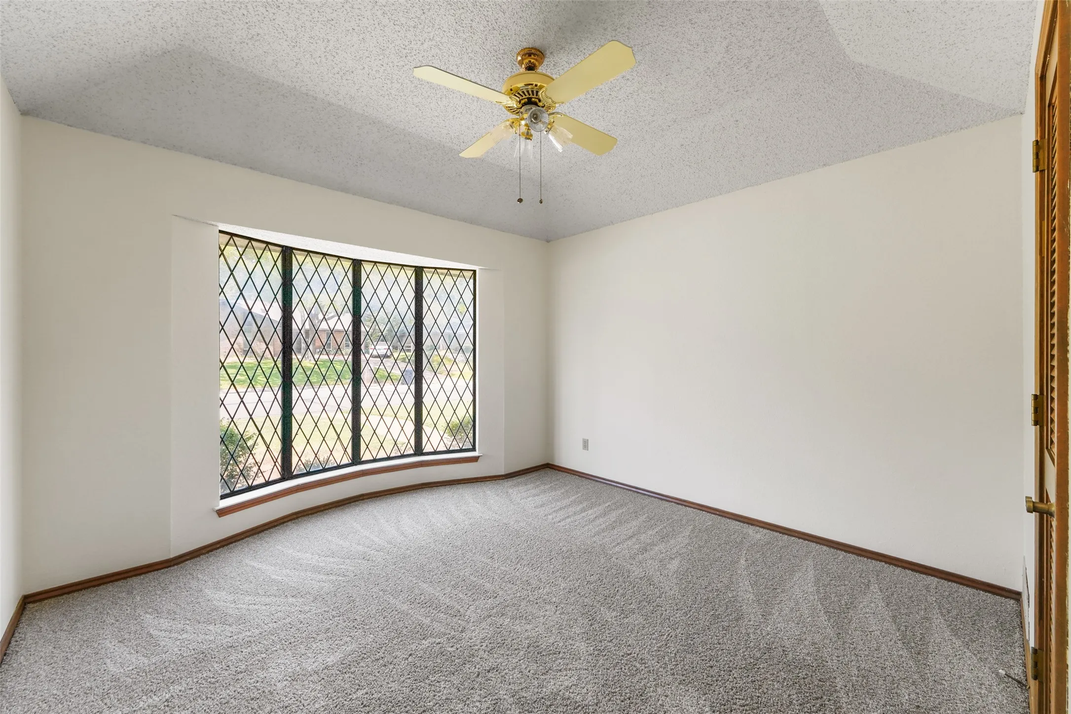 Curved bay window with diamond-pattern grilles, textured ceiling, ceiling fan, and light-toned wall-to-wall carpeting