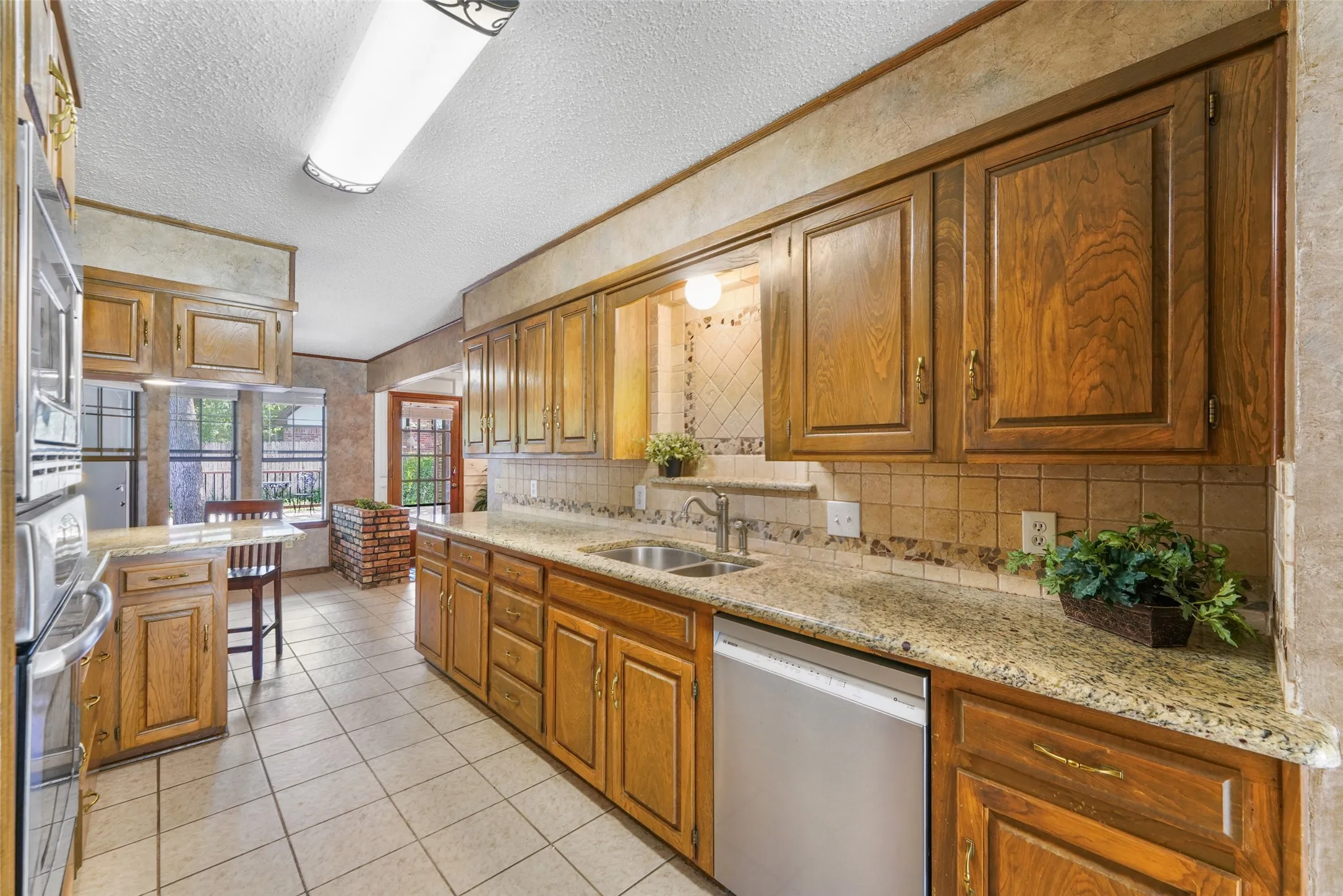 Kitchen featuring wood cabinetry, granite countertops, tile flooring, and integrated stainless steel appliances