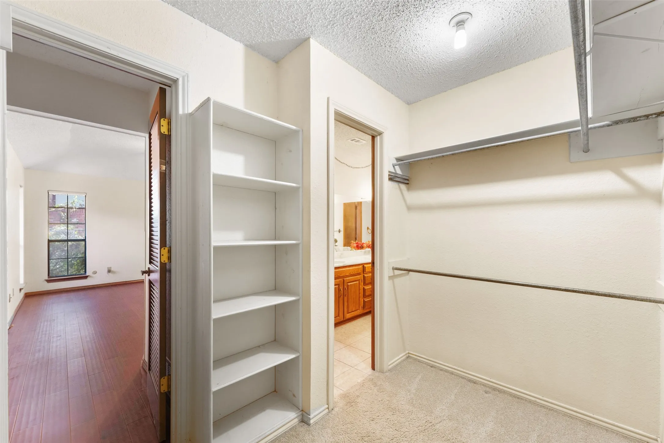 Built-in shelving, hanging rods, and carpet flooring in this closet space, with wood-finish flooring visible in the adjacent room