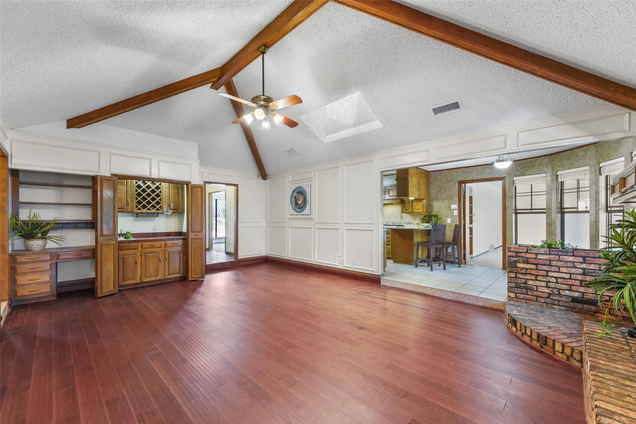 Vaulted ceiling with exposed wood beams, wood-finish flooring, built-in wet bar, and a brick planter