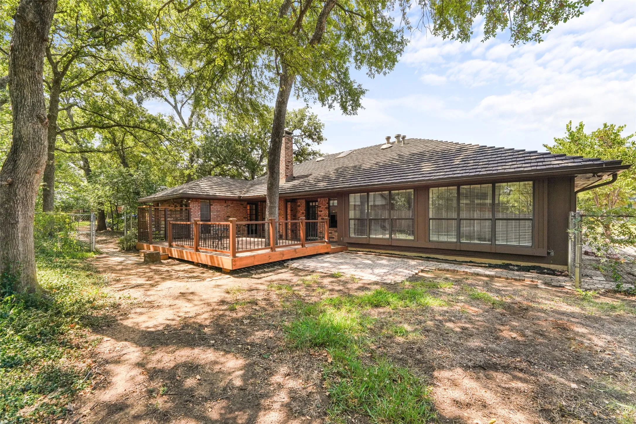 Expansive rear elevation featuring a wood deck, brick exterior, and a series of floor-to-ceiling windows