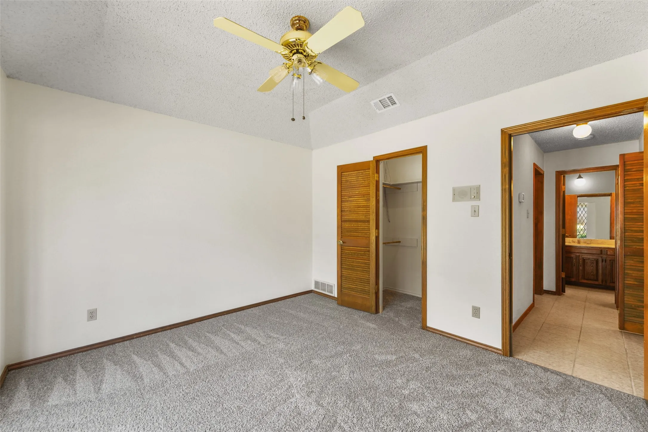 Neutral tone wall finish, textured ceiling, ceiling fan with integrated lighting, wood-finish interior doors, and gray carpet
