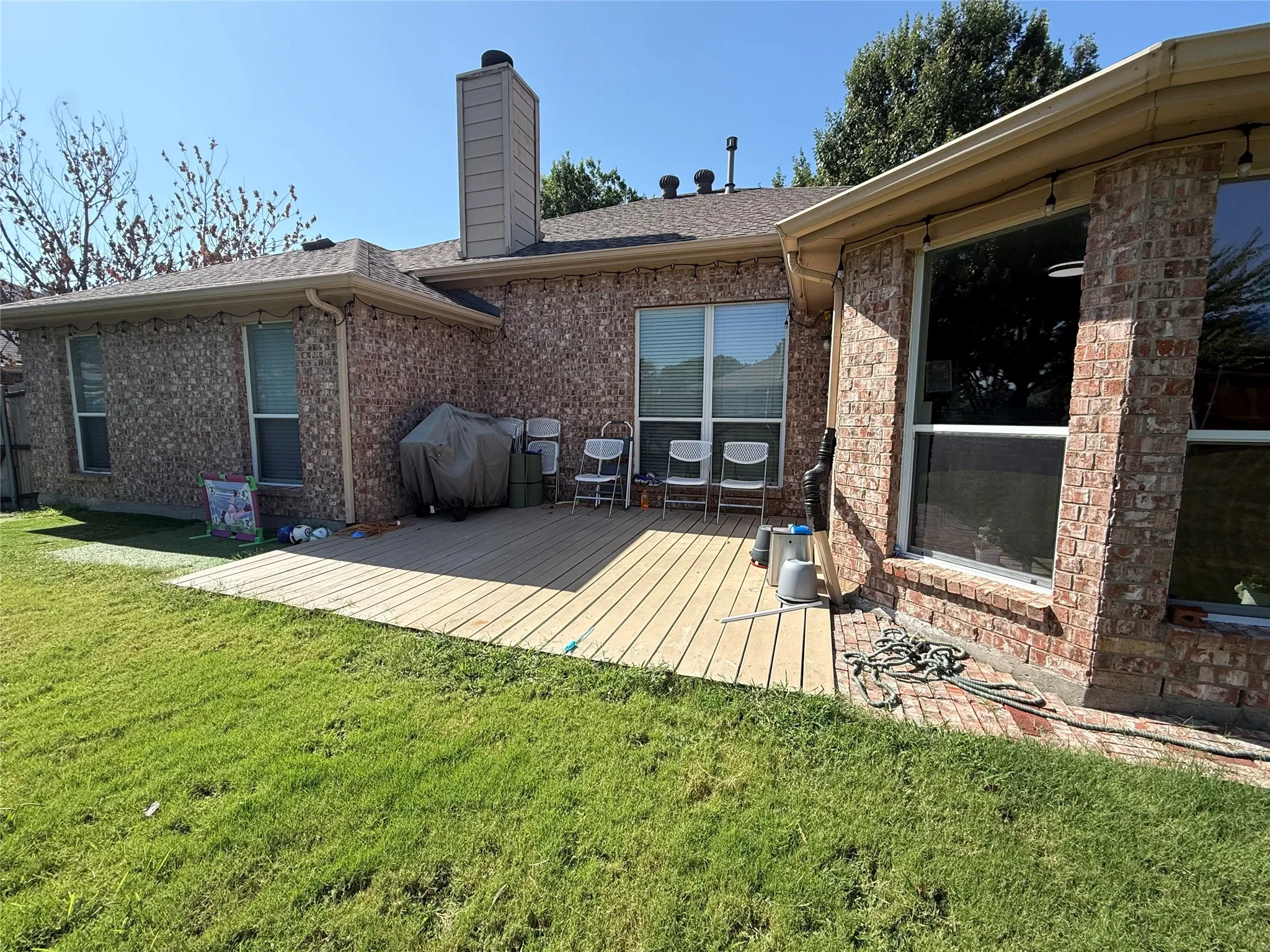 Brick exterior home with expansive composite deck overlooking manicured lawn and mature landscaping