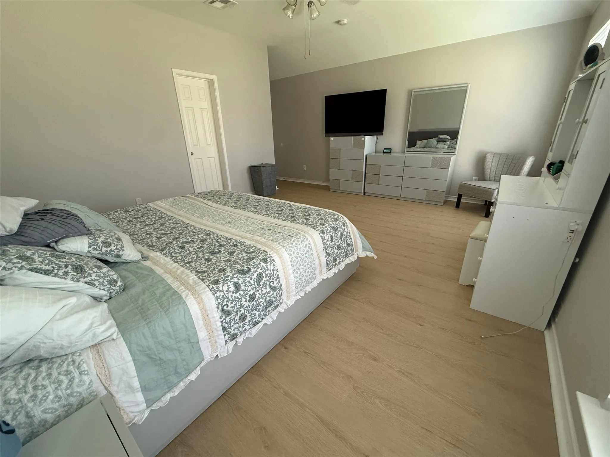Vaulted ceiling, light-toned wood-finish flooring, white trim, and a white paneled door