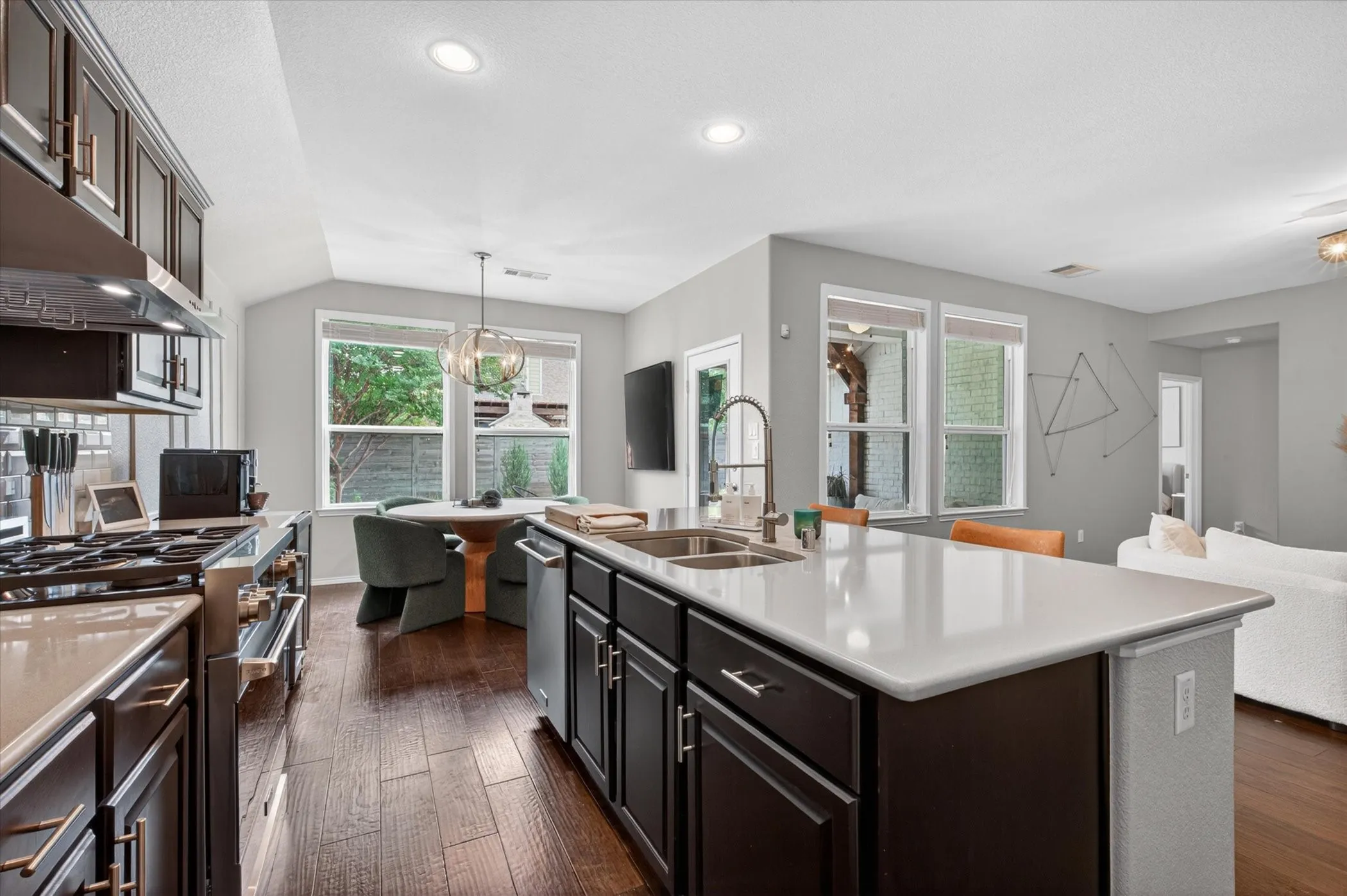 Contemporary kitchen featuring a spacious island with an undermount sink, dark wood-finish cabinetry, light countertops, and stainless steel appliances