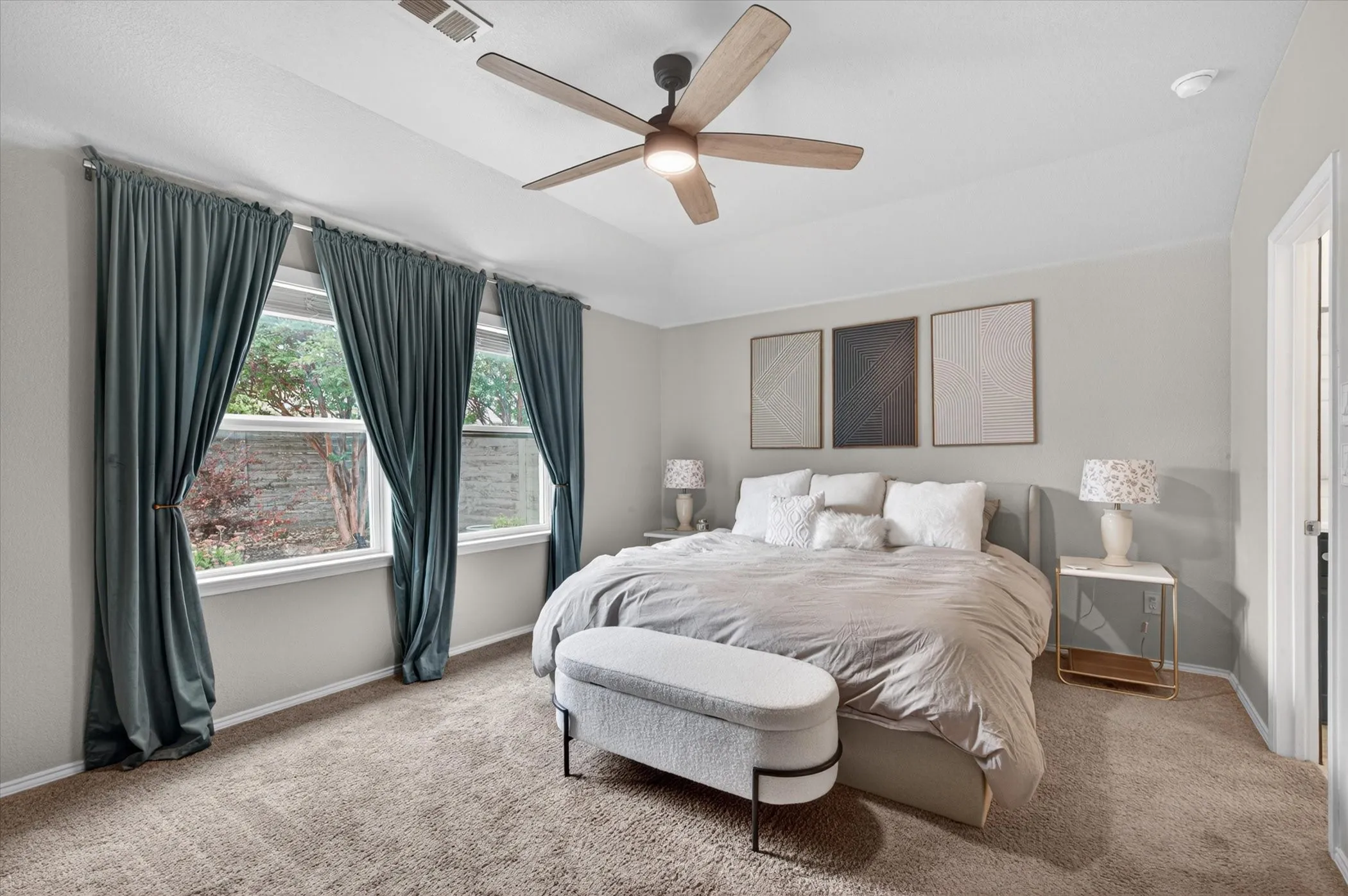Carpeted room featuring a ceiling fan, three windows with curtains, and a white door frame