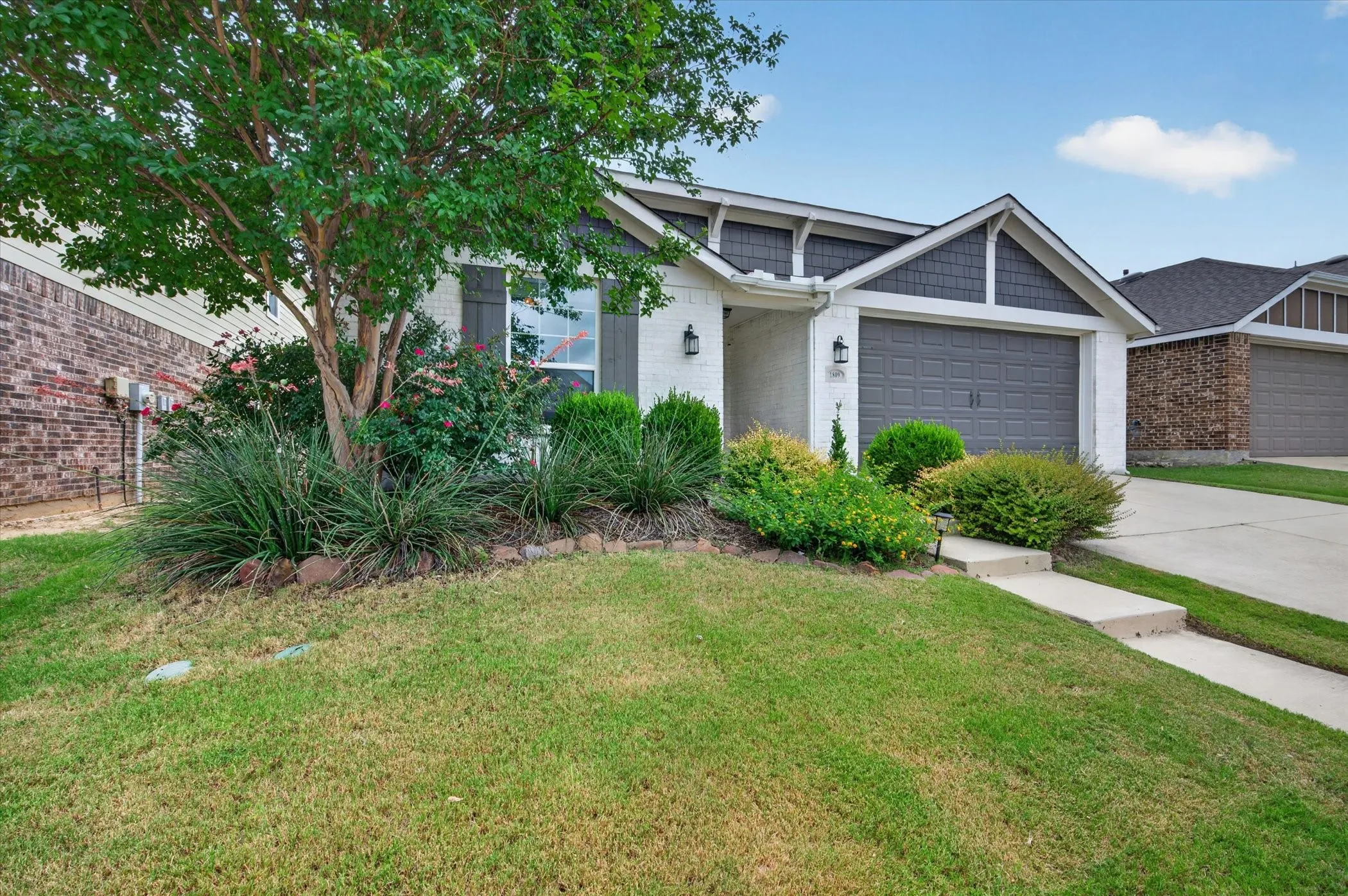 White brick exterior with dark gray siding accents, attached two-car garage, concrete driveway, and established front landscaping