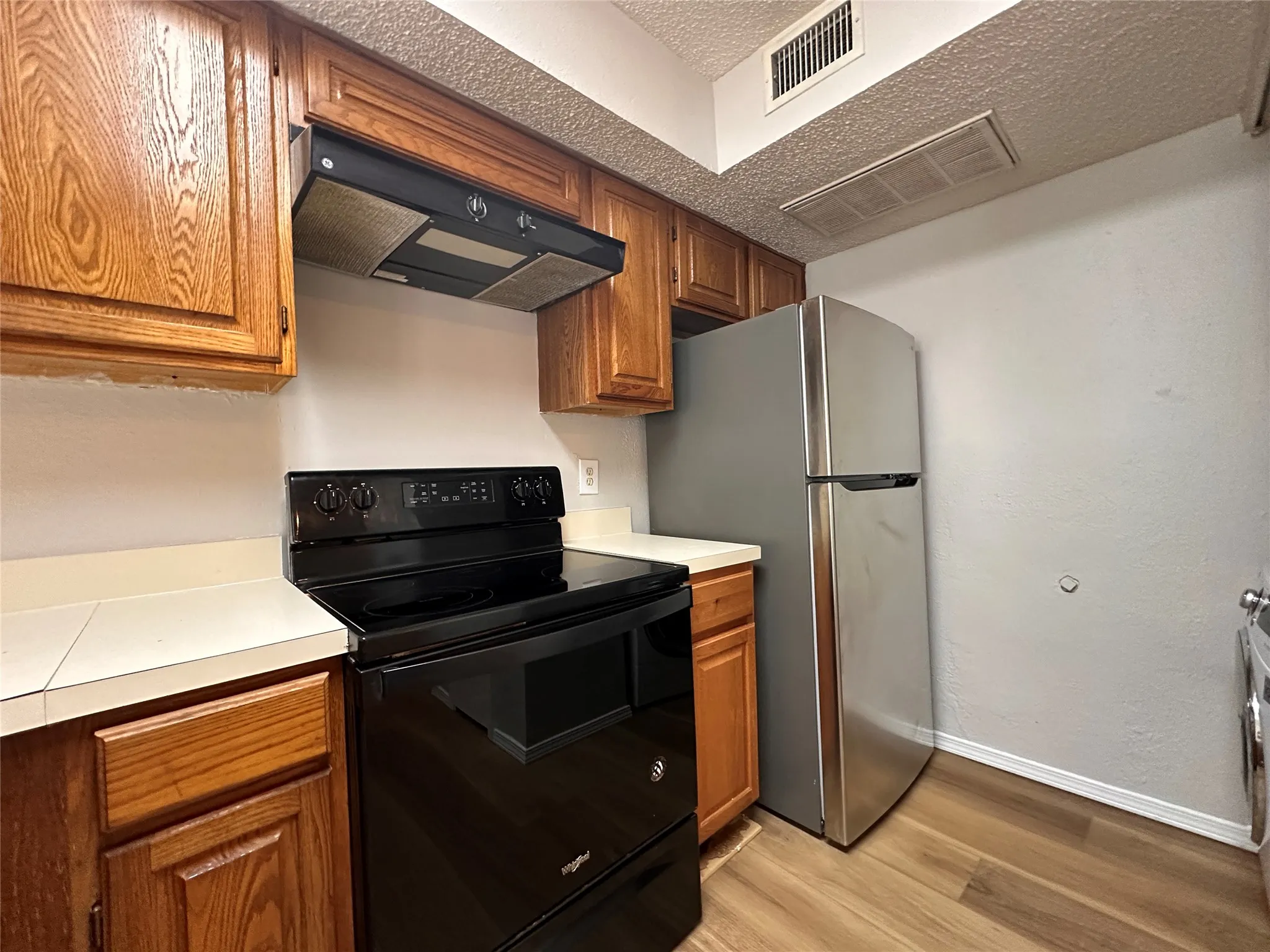 Kitchen featuring premium range hood, black / electric stove, a textured ceiling, stainless steel fridge, and light wood-type flooring