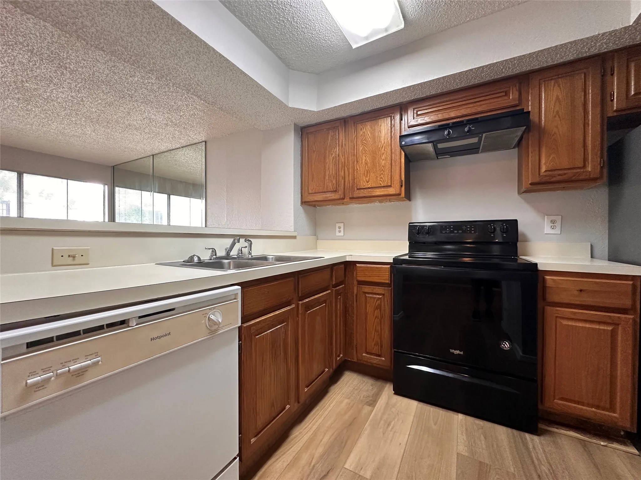 Kitchen featuring a textured ceiling, black range with electric stovetop, dishwasher, light hardwood / wood-style floors, and premium range hood