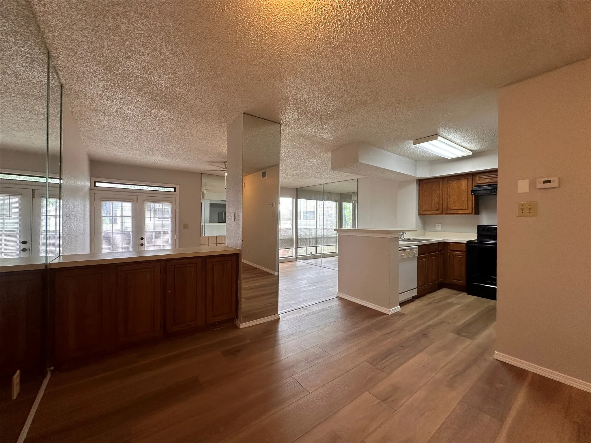 Kitchen featuring light wood-type flooring, black range with electric cooktop, kitchen peninsula, white dishwasher, and a textured ceiling