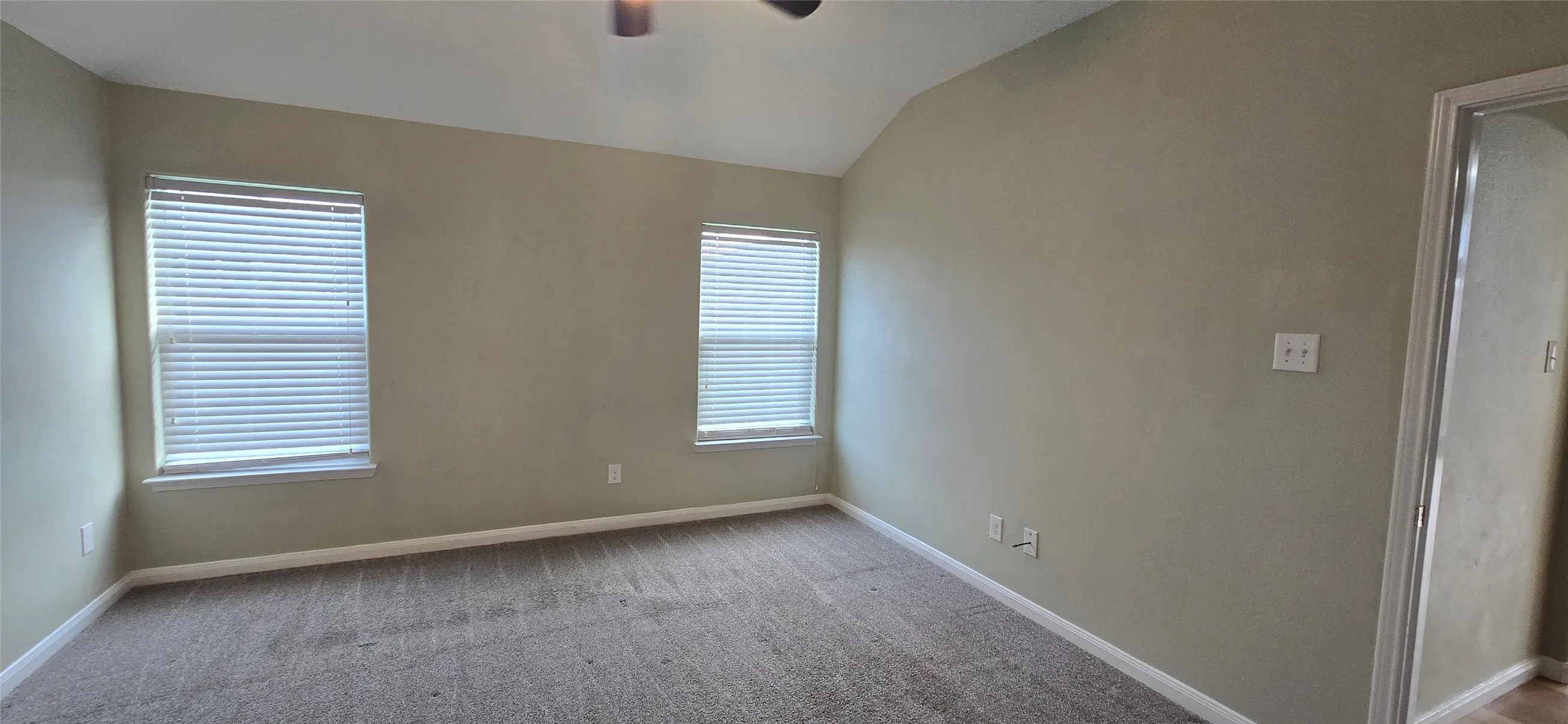 Carpeted spare room featuring baseboards, lofted ceiling, and a ceiling fan