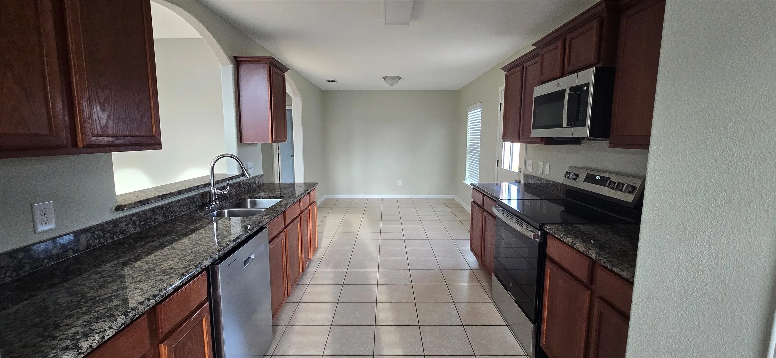 Kitchen with light tile patterned floors, dark stone countertops, baseboards, a sink, and appliances with stainless steel finishes