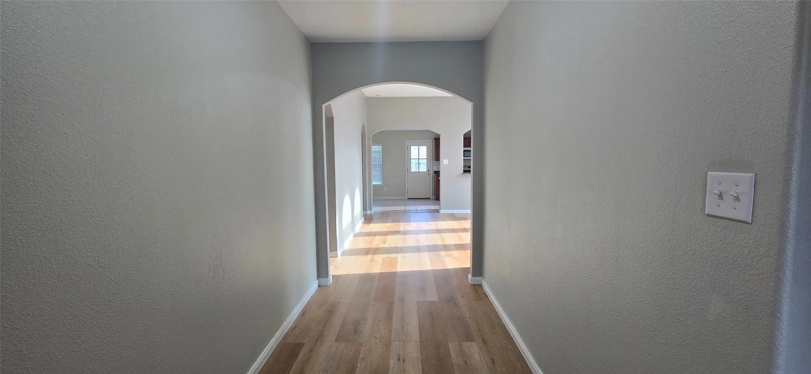 Corridor featuring a textured wall, arched walkways, baseboards, and wood finished floors