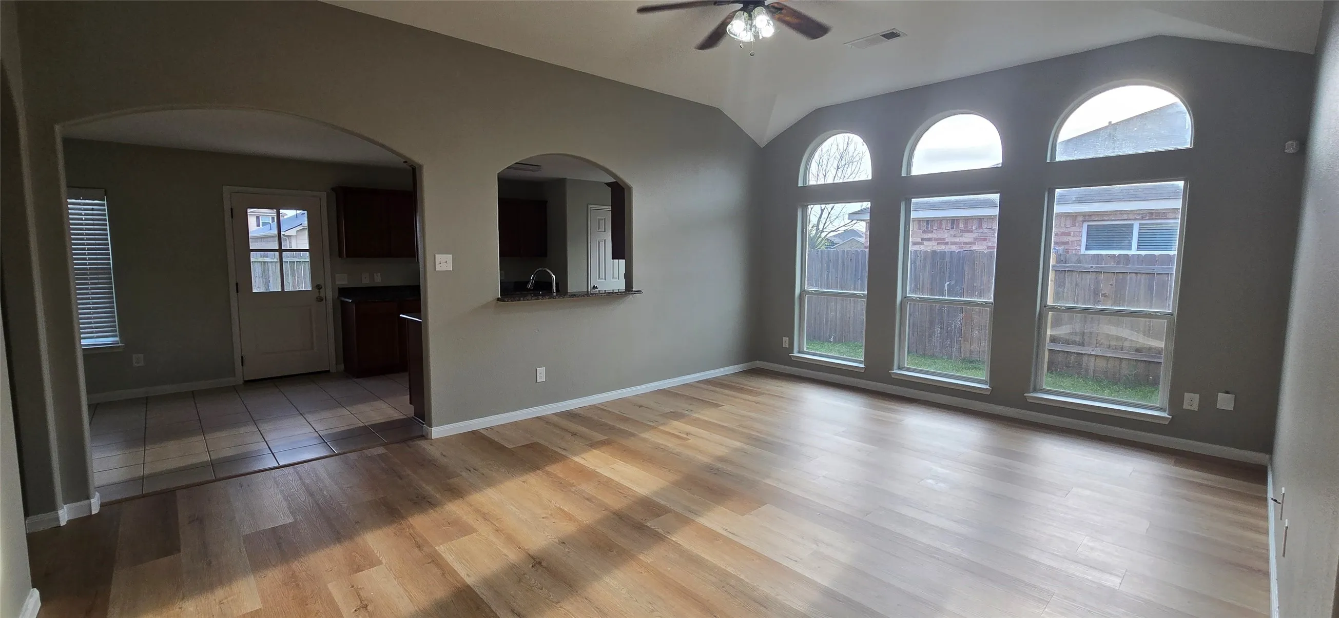 Empty room featuring visible vents, light wood finished floors, ceiling fan, a sink, and vaulted ceiling