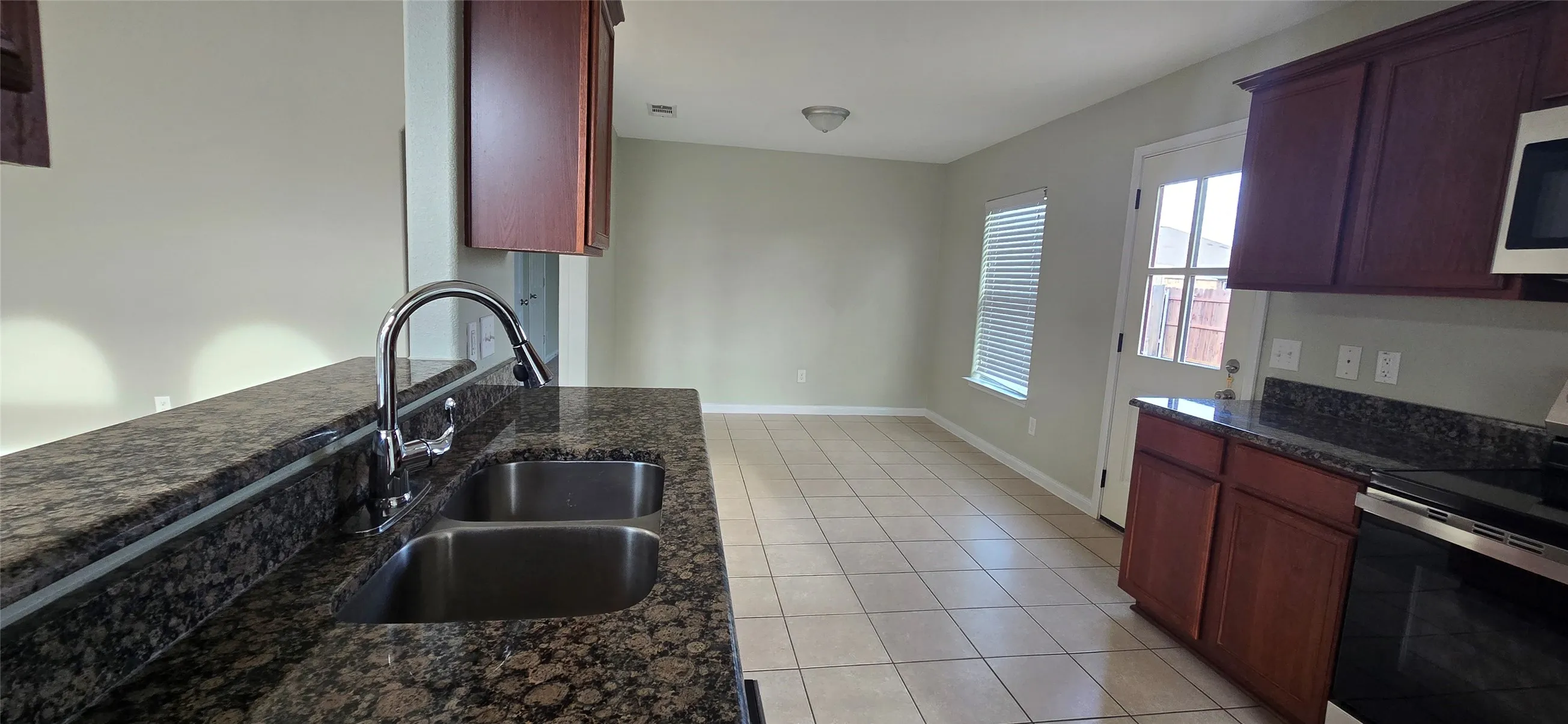 Kitchen with reddish brown cabinets, a sink, light tile patterned floors, baseboards, and stainless steel electric stove