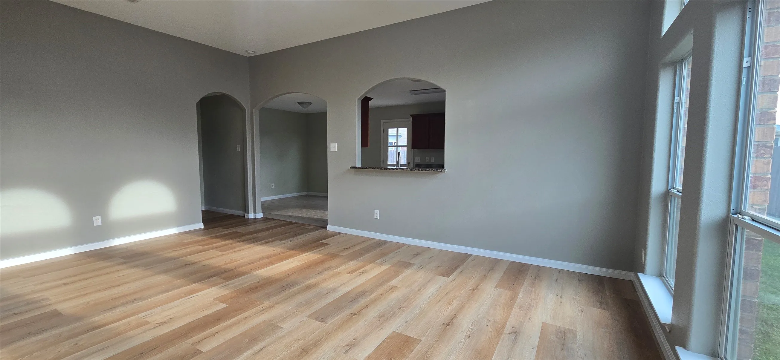 Empty room featuring arched walkways, baseboards, and light wood finished floors