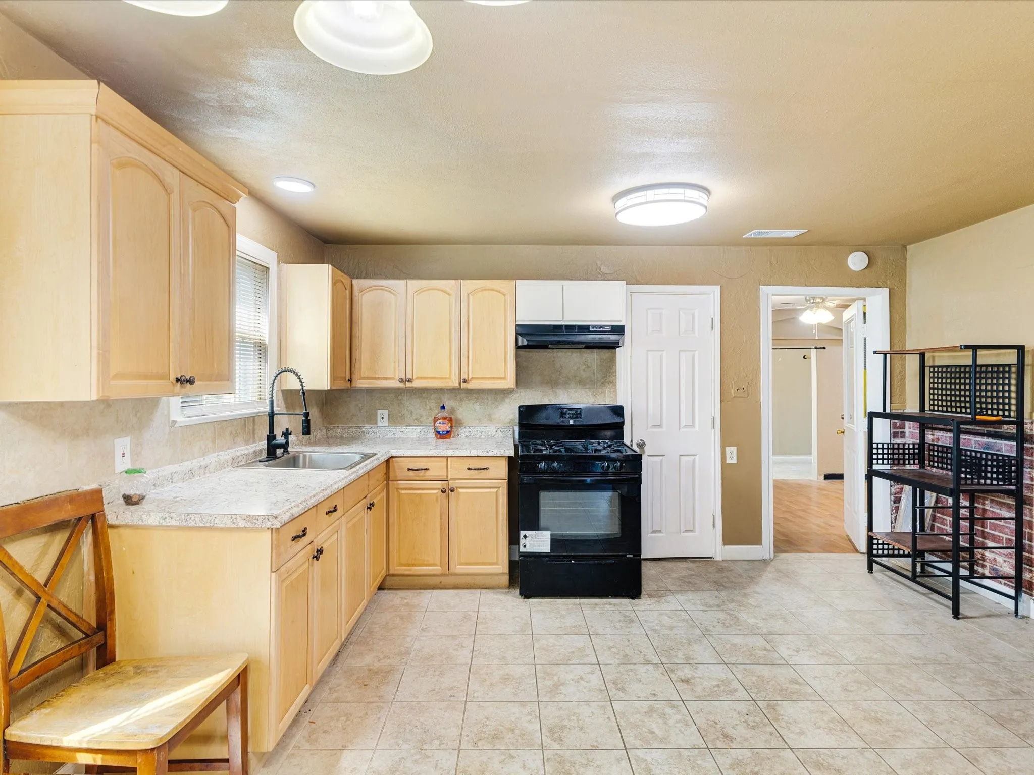 Kitchen featuring light wood-finish cabinetry, light-toned countertops, tile flooring, a black range, and a stainless steel sink with a black faucet