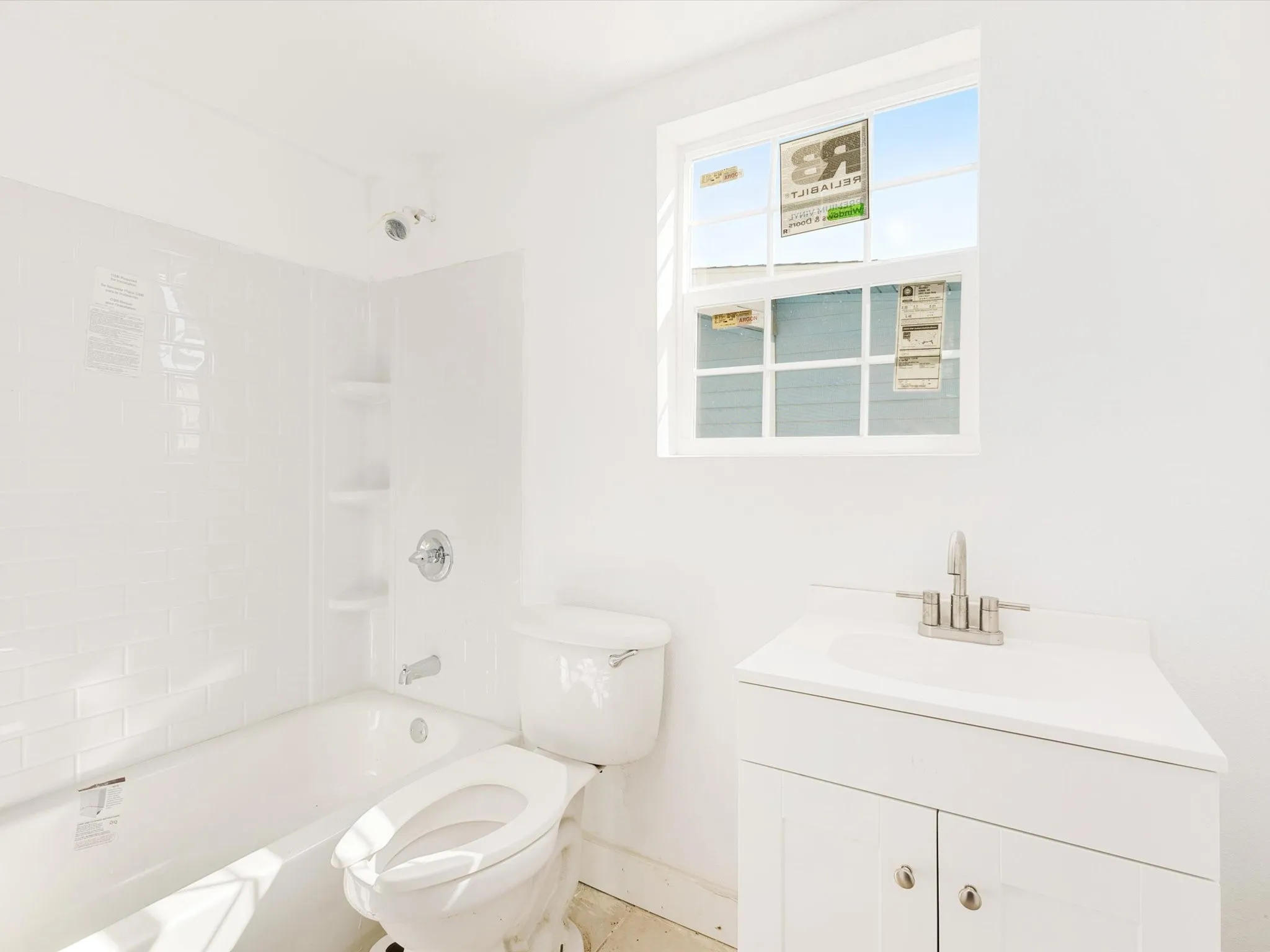White subway tile bath/shower surround with built-in shelving, chrome fixtures, single pane window, and a white vanity with a single basin sink