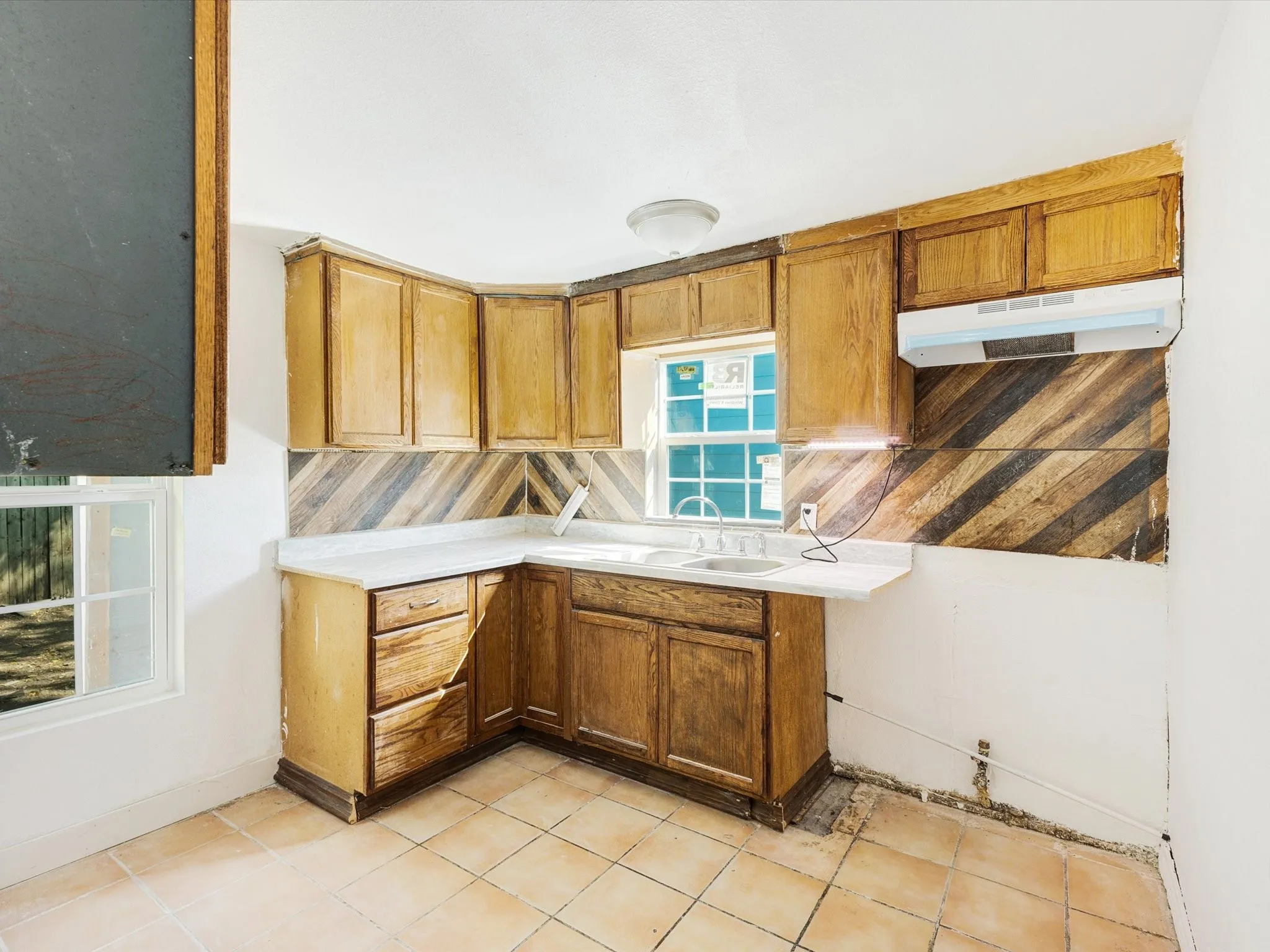 Corner kitchen layout with wood cabinetry, light-toned countertops, and a double basin sink