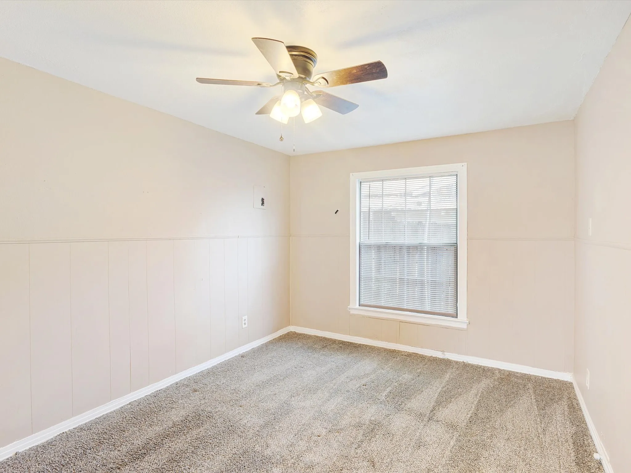 Bright bedroom with neutral wall finishes, carpeted flooring, ceiling fan with integrated lighting, and large double-hung window providing natural light