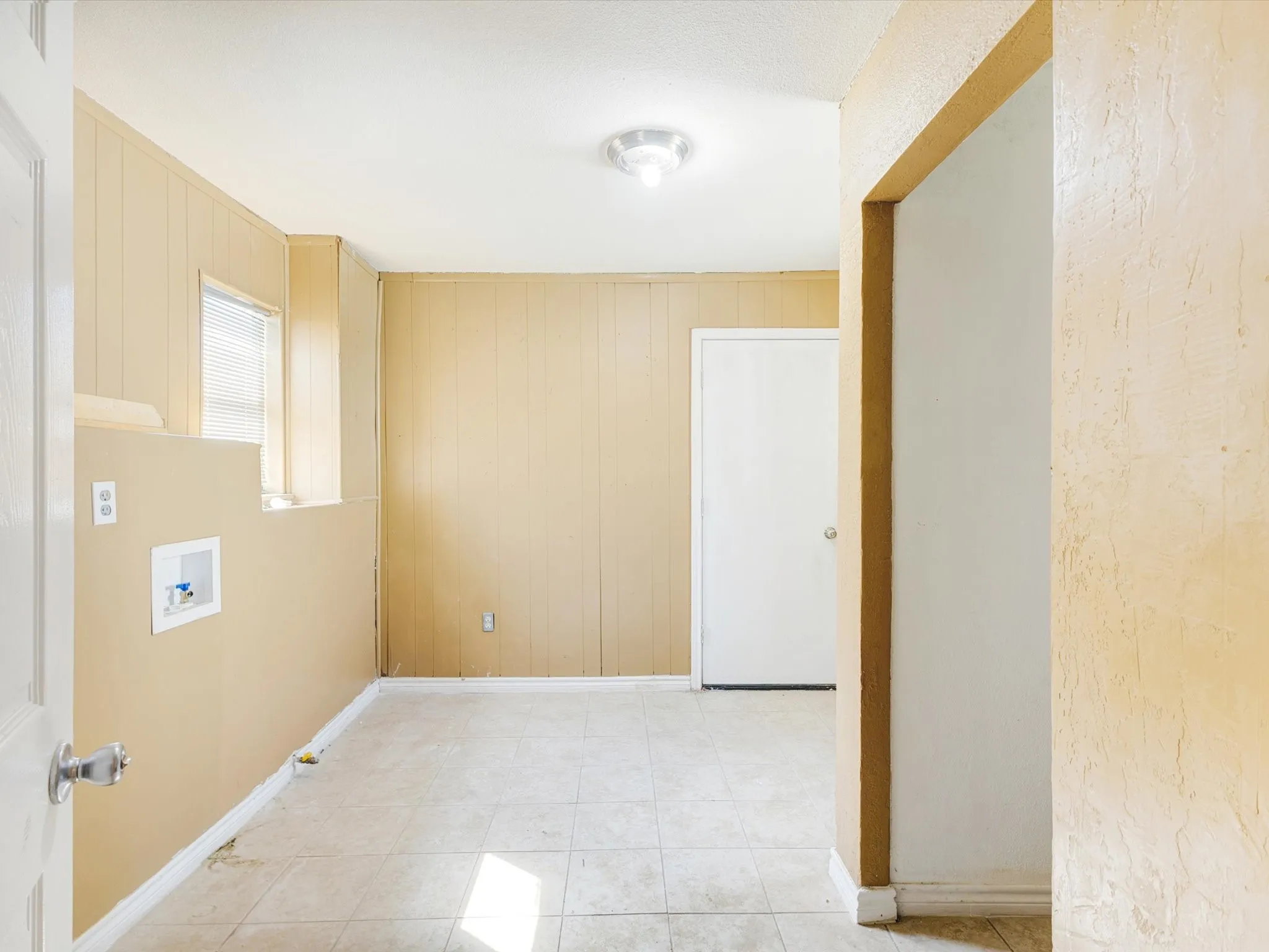Recessed window with blinds, paneling, tile flooring, and utility hookups