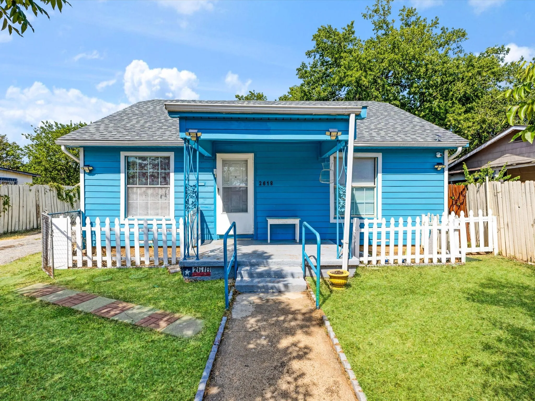 Vibrant blue exterior siding with a covered porch entry, a white picket fence, and a green lawn