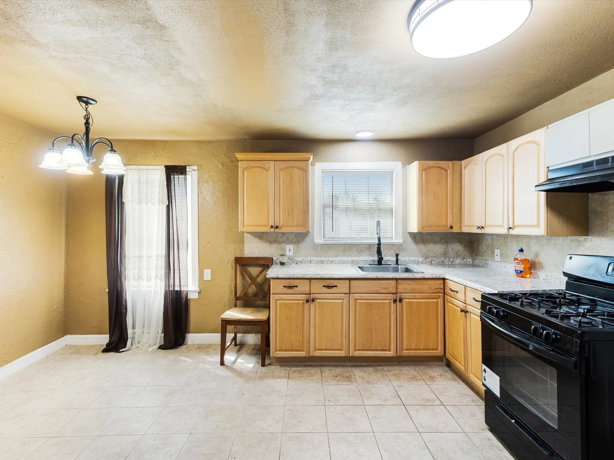 Spacious kitchen featuring warm wood-finish cabinetry, stainless steel gas range with dual ovens, ceramic tile flooring, and a center island with seating