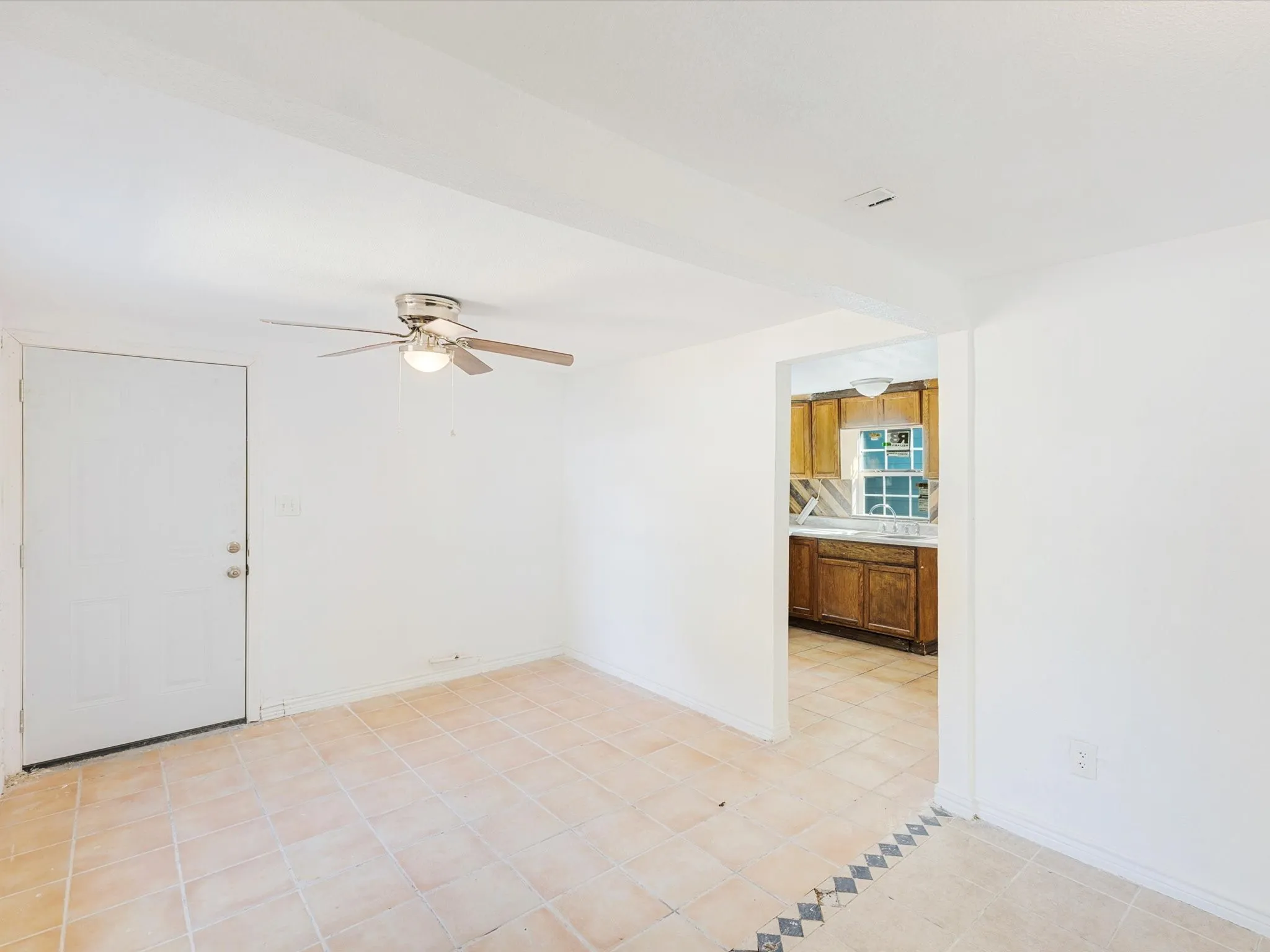 Tile flooring with a decorative border, ceiling fan with light fixture, and a doorway opening to a kitchen with wood cabinetry