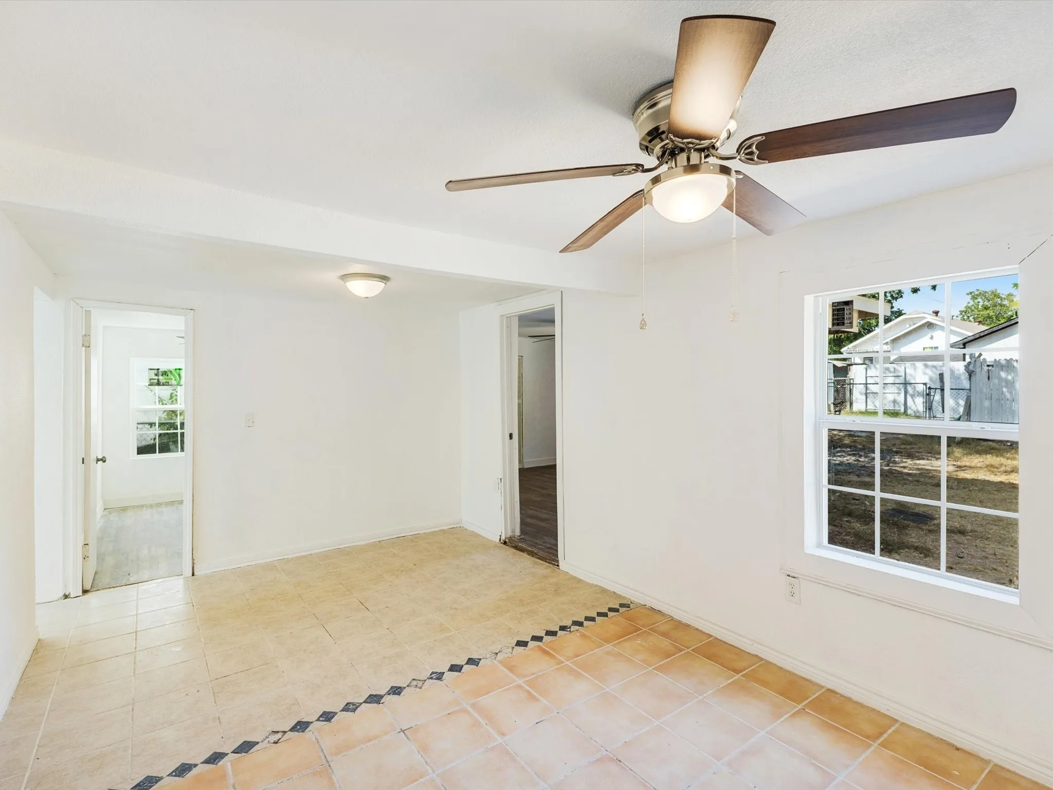 Tiled flooring with decorative border, white walls, flush mount lighting, a window, and a ceiling fan with integrated light