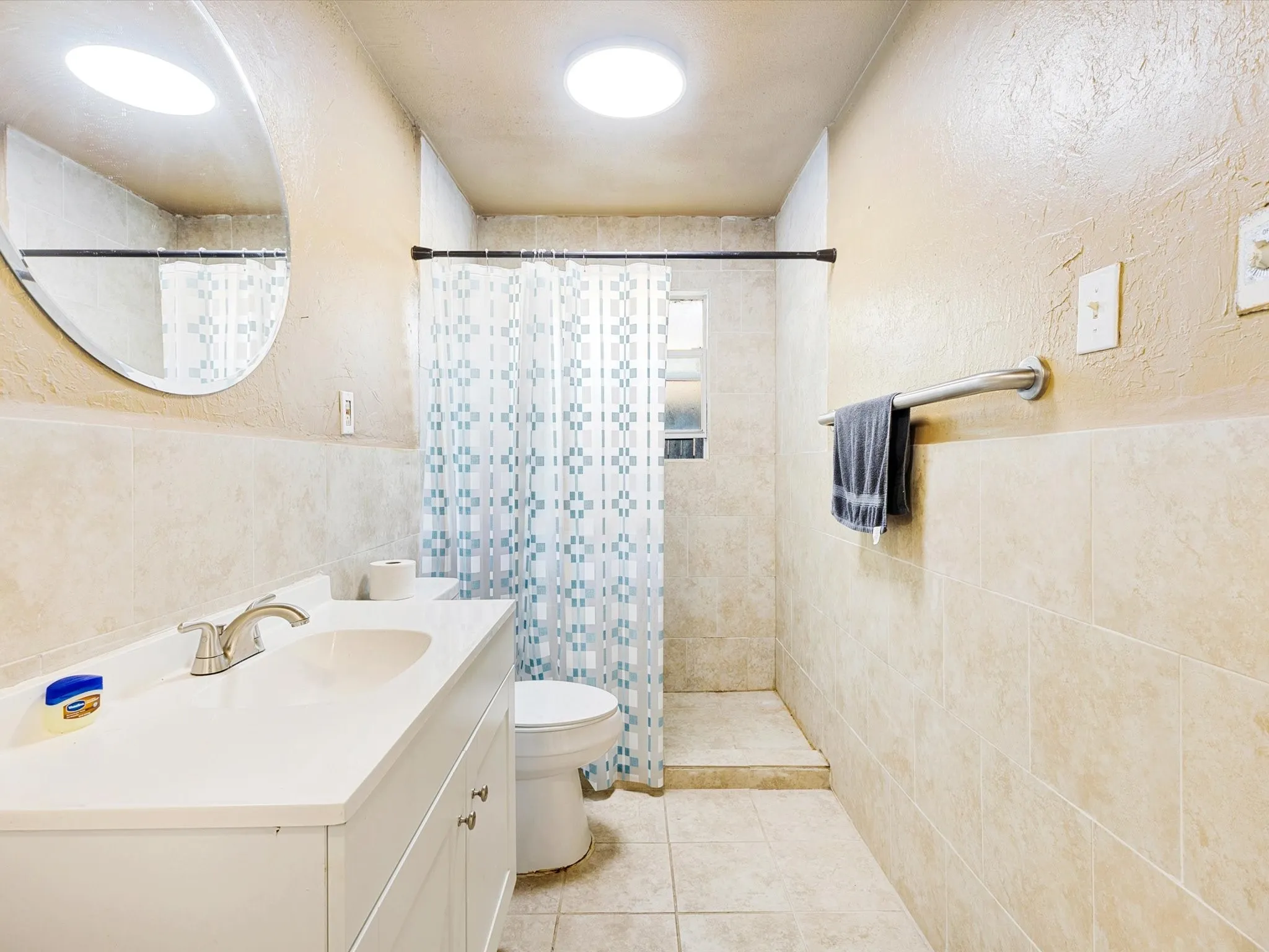 Bright, updated bathroom featuring a spacious vanity with ample counter space, recessed ceiling lighting, a walk-in shower with tiled surround and glass enclosure, ceramic tile flooring, and brushed metal towel bar and hardware