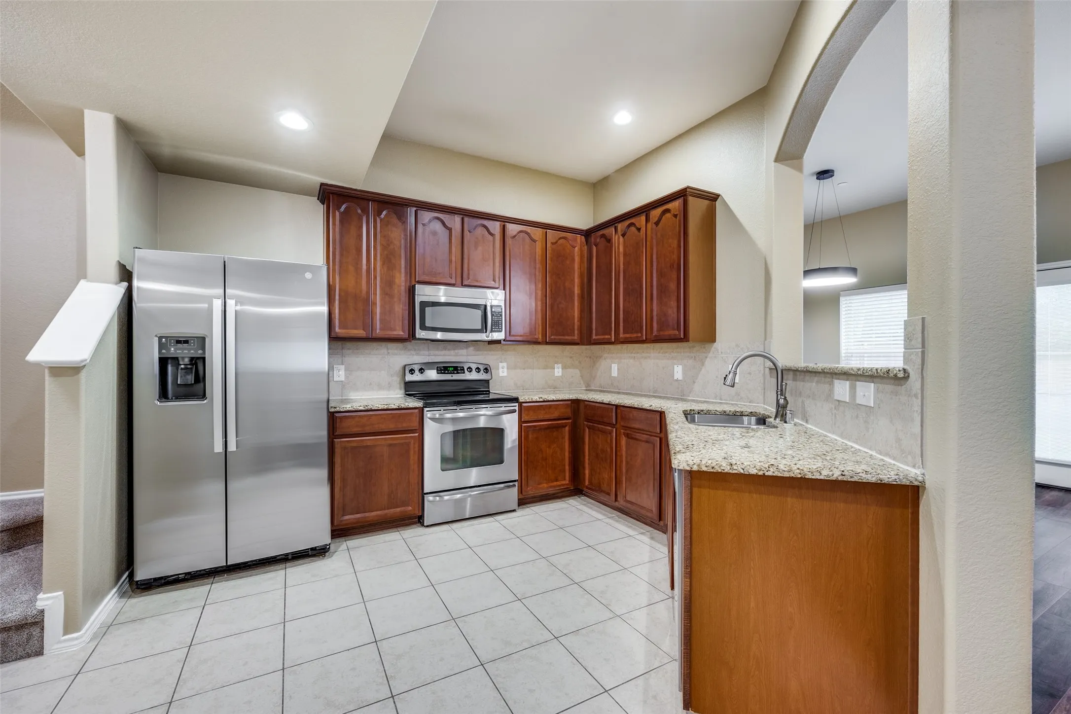 Kitchen featuring stainless steel appliances, granite countertops, tile flooring, wood cabinetry, and recessed lighting