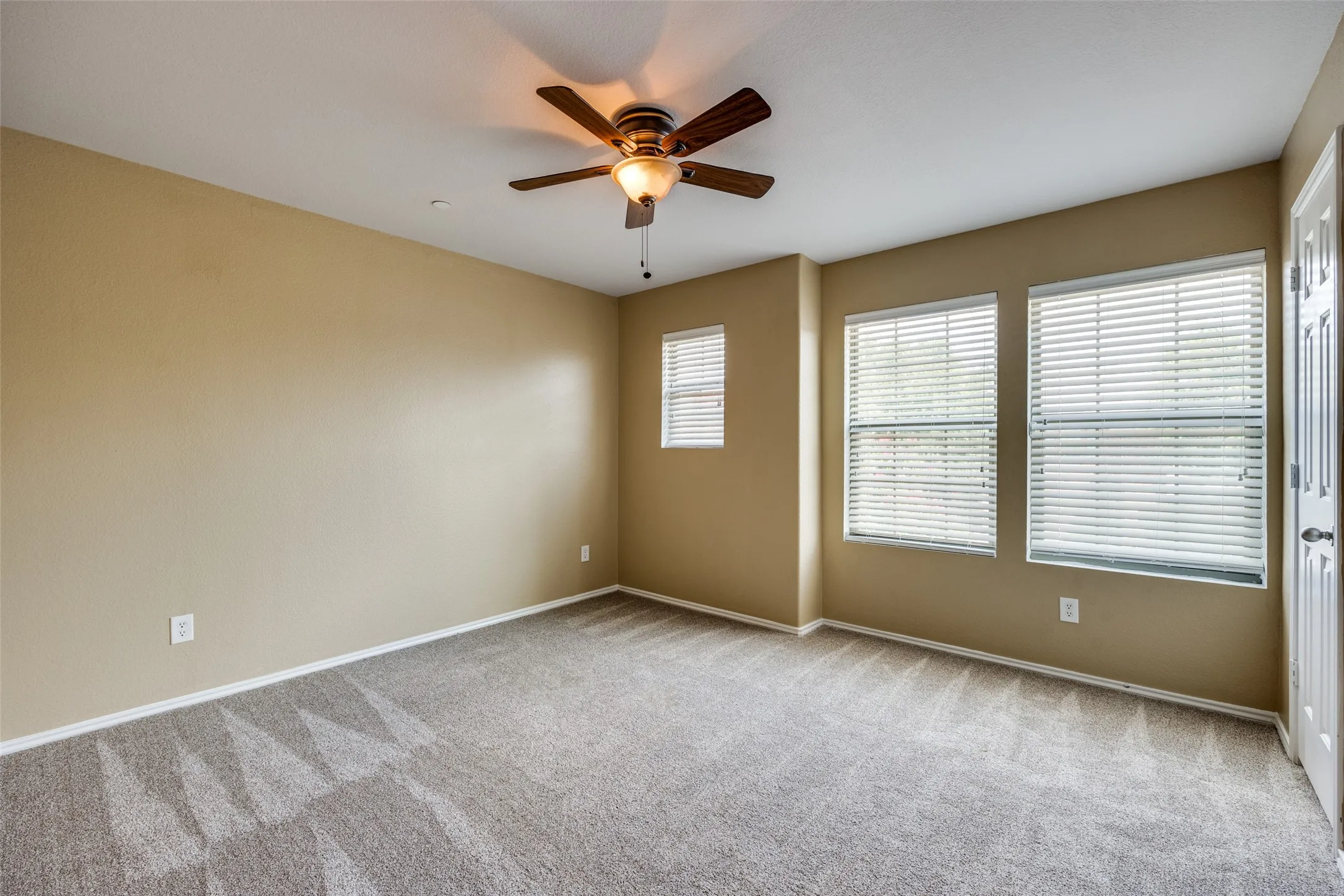 Carpeted flooring, ceiling fan with integrated lighting, multiple windows with horizontal blinds, and neutral-toned walls