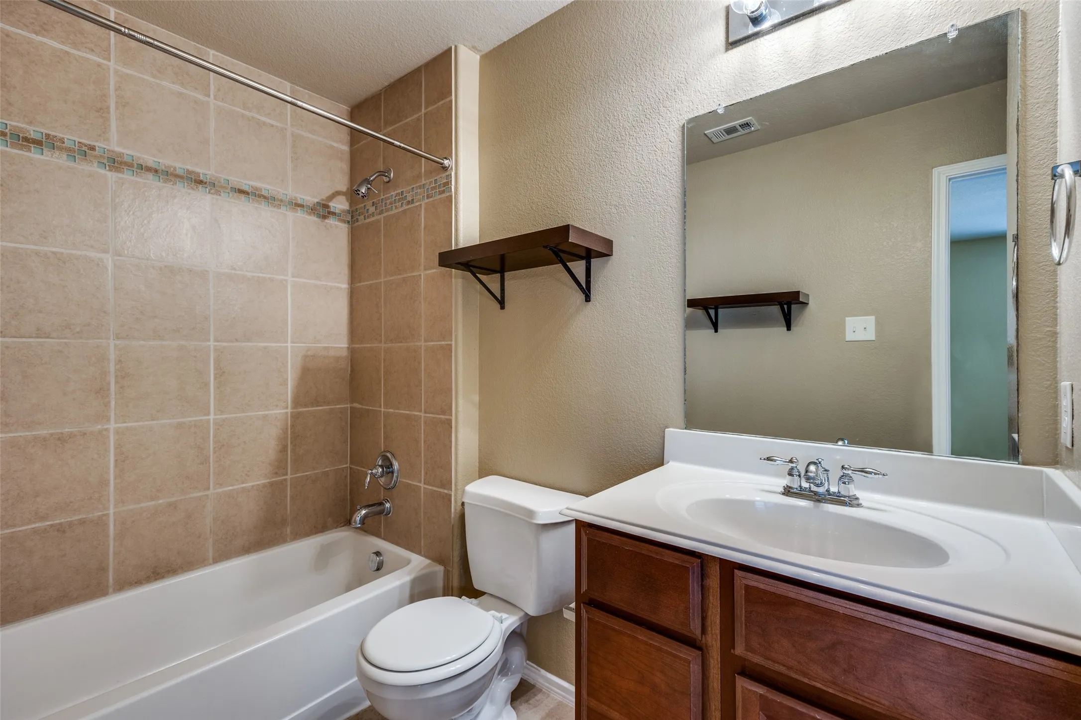 Enclosed bathroom featuring a full bathtub with tiled surround, a toilet, a single vanity with an integrated sink, and a wall-mounted mirror
