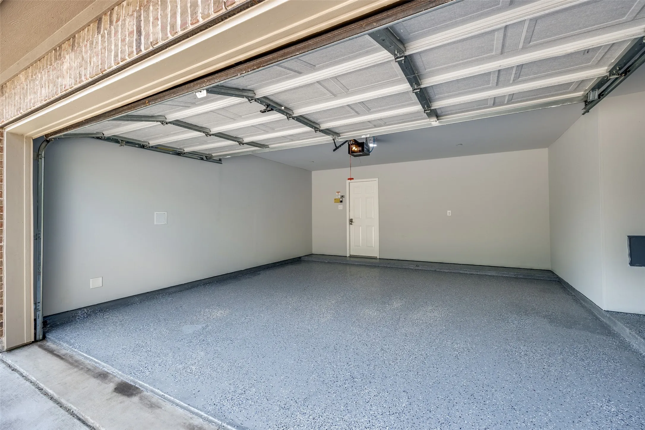 Garage with epoxy-coated concrete flooring, painted walls, and an overhead door opener