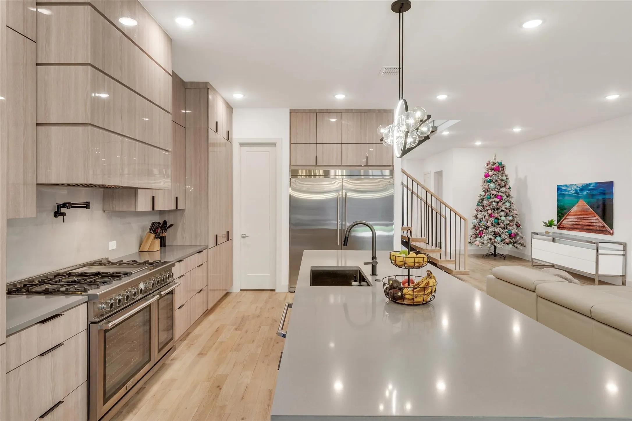 Chef's kitchen featuring custom wood-finish cabinetry, professional-grade dual ovens, gas cooktop, stainless steel appliances, and a generous quartz island with waterfall edge