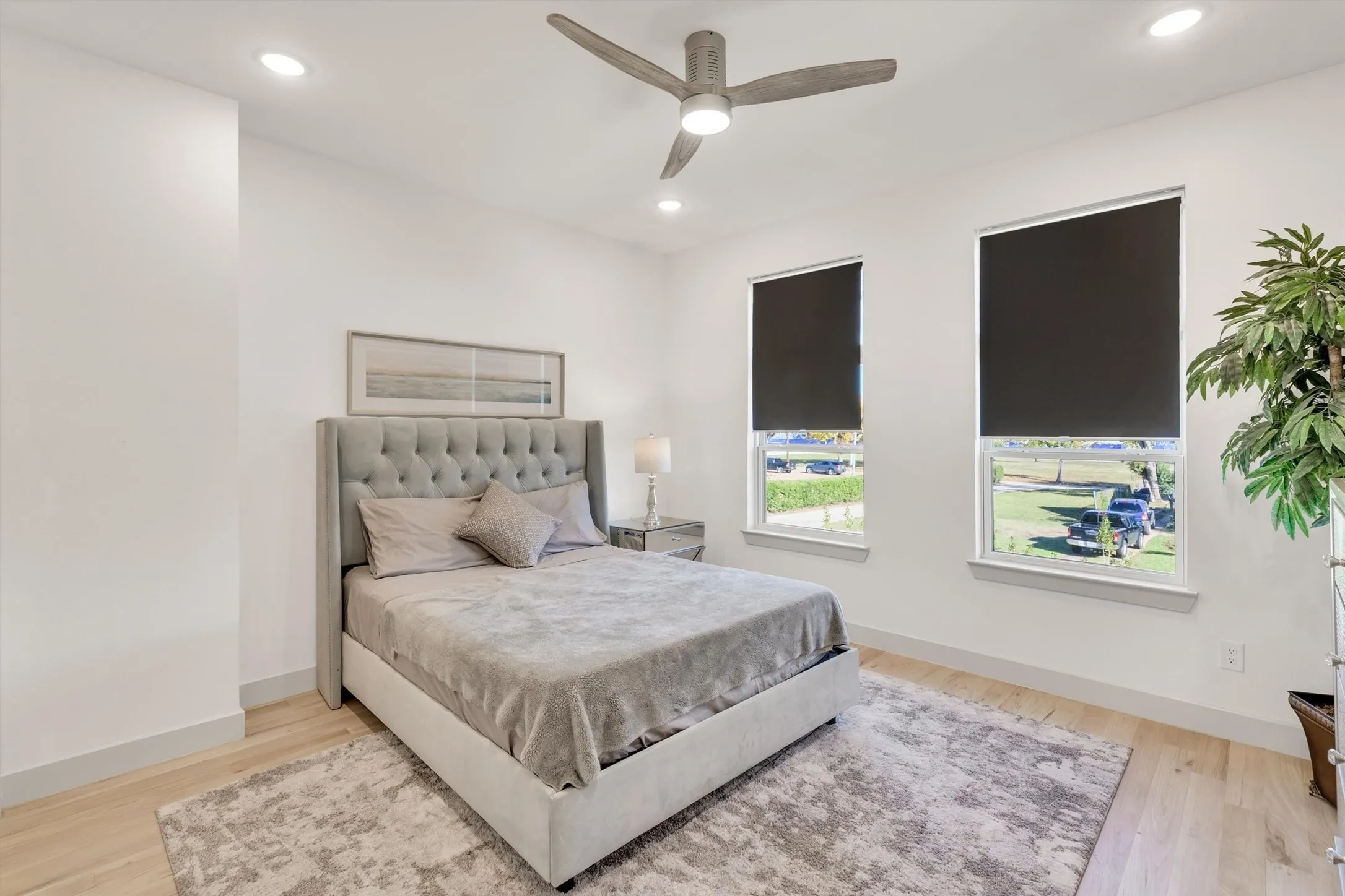 Recessed lighting, wood-finish flooring, two windows with roller shades, and a ceiling fan with integrated lighting