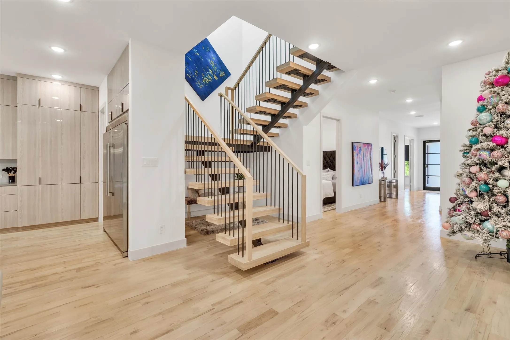Floating staircase with metal balusters, light wood-finish flooring, recessed lighting, integrated refrigerator, and light wood-finish cabinetry