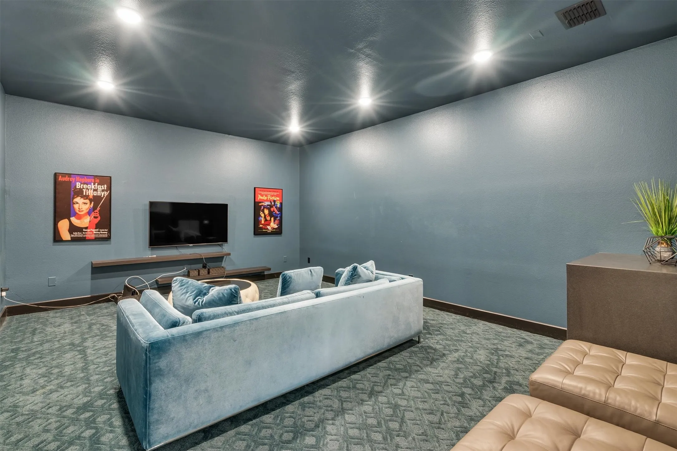 Recessed ceiling lighting, wall-mounted television, built-in floating media console, and patterned carpeting with a dark baseboard